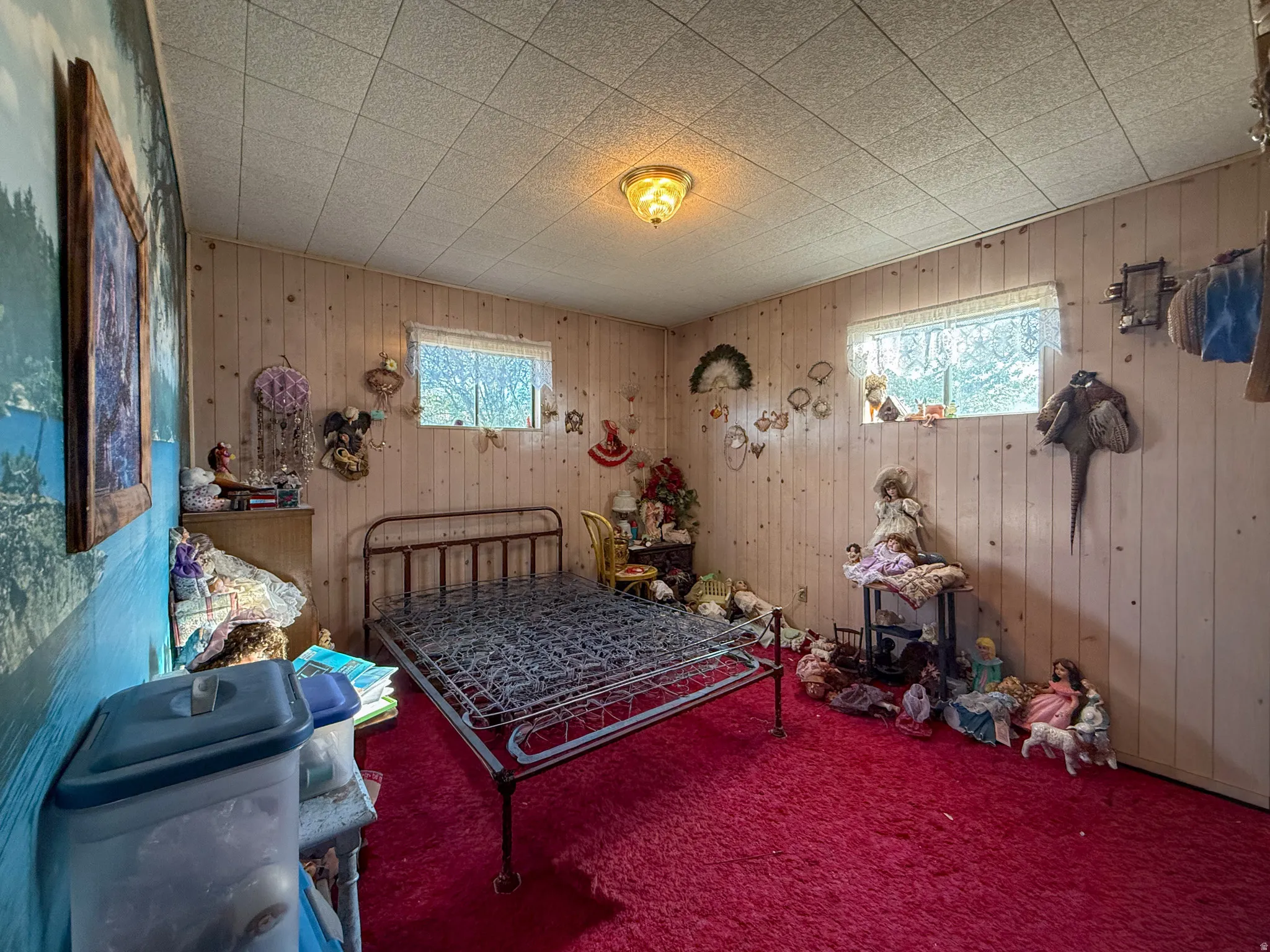 Room featuring wood paneling on three walls, a deep red carpet, and a drop ceiling