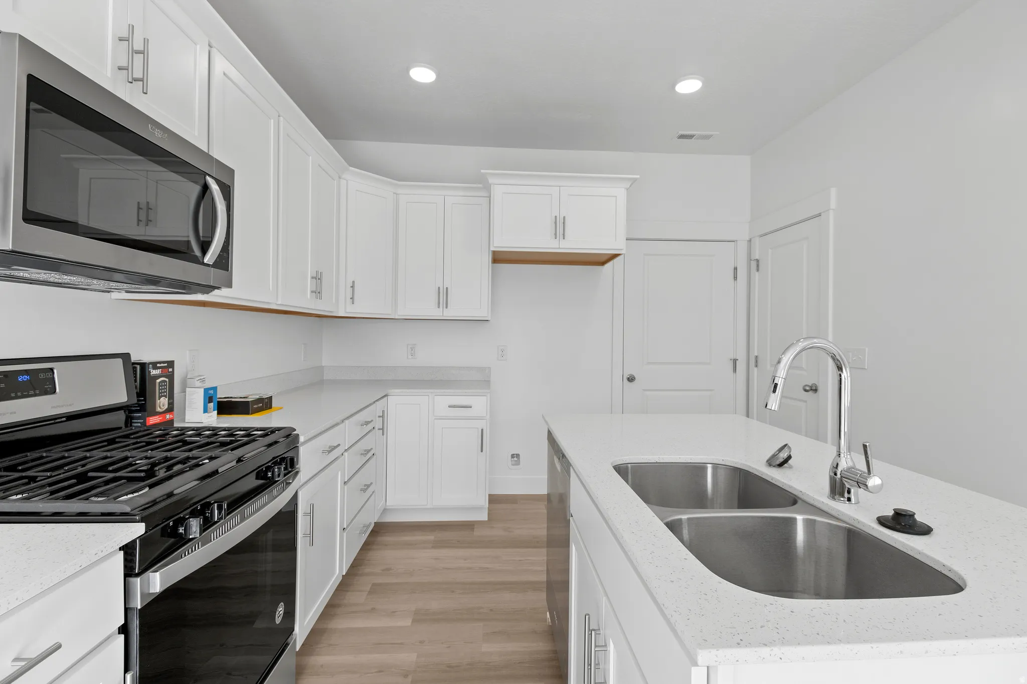 Modern kitchen featuring white cabinetry, light-toned countertops, stainless steel appliances, and wood-finish flooring