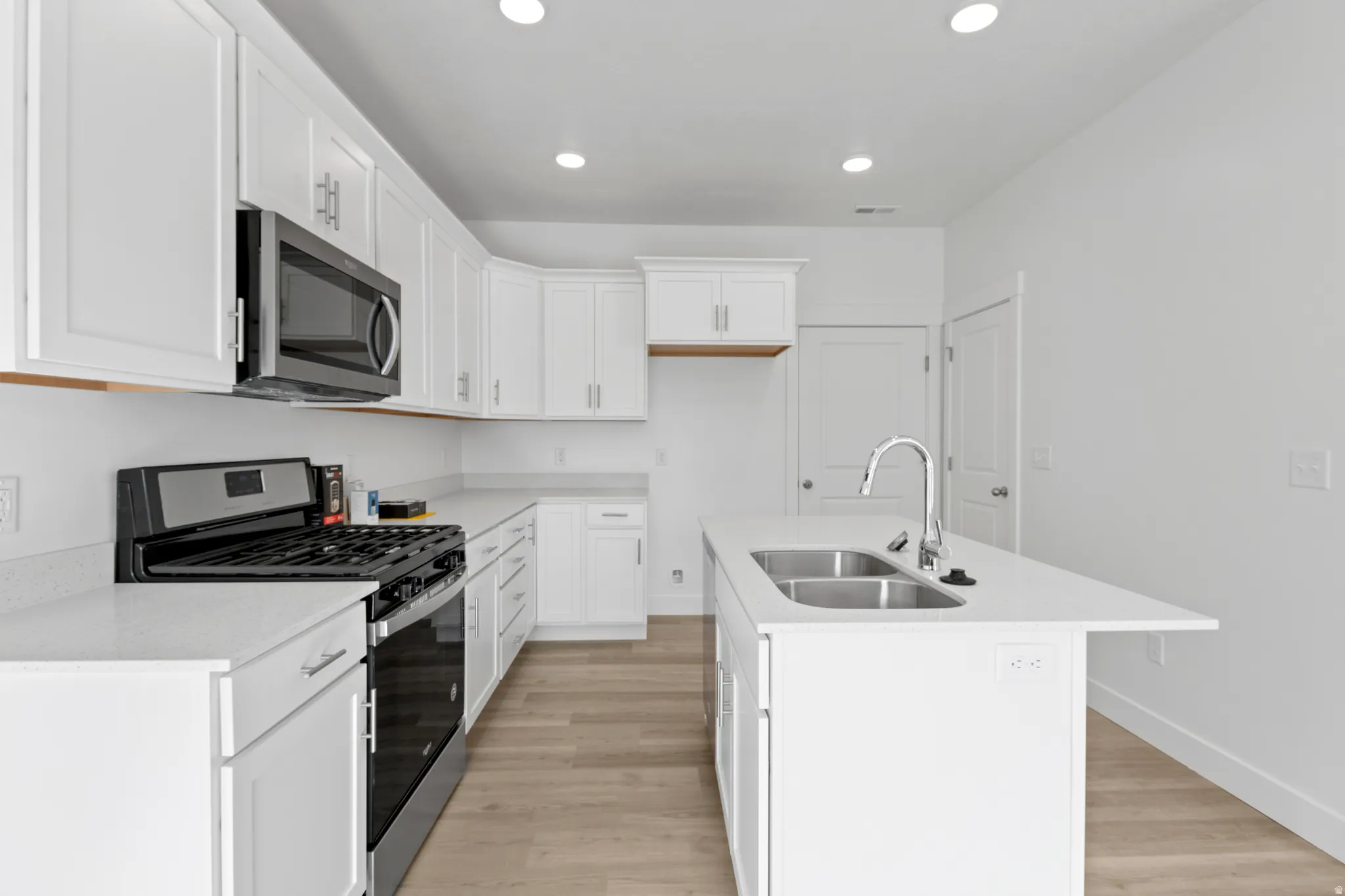 Modern kitchen with white cabinetry, stainless steel appliances, and light-toned wood-finish flooring