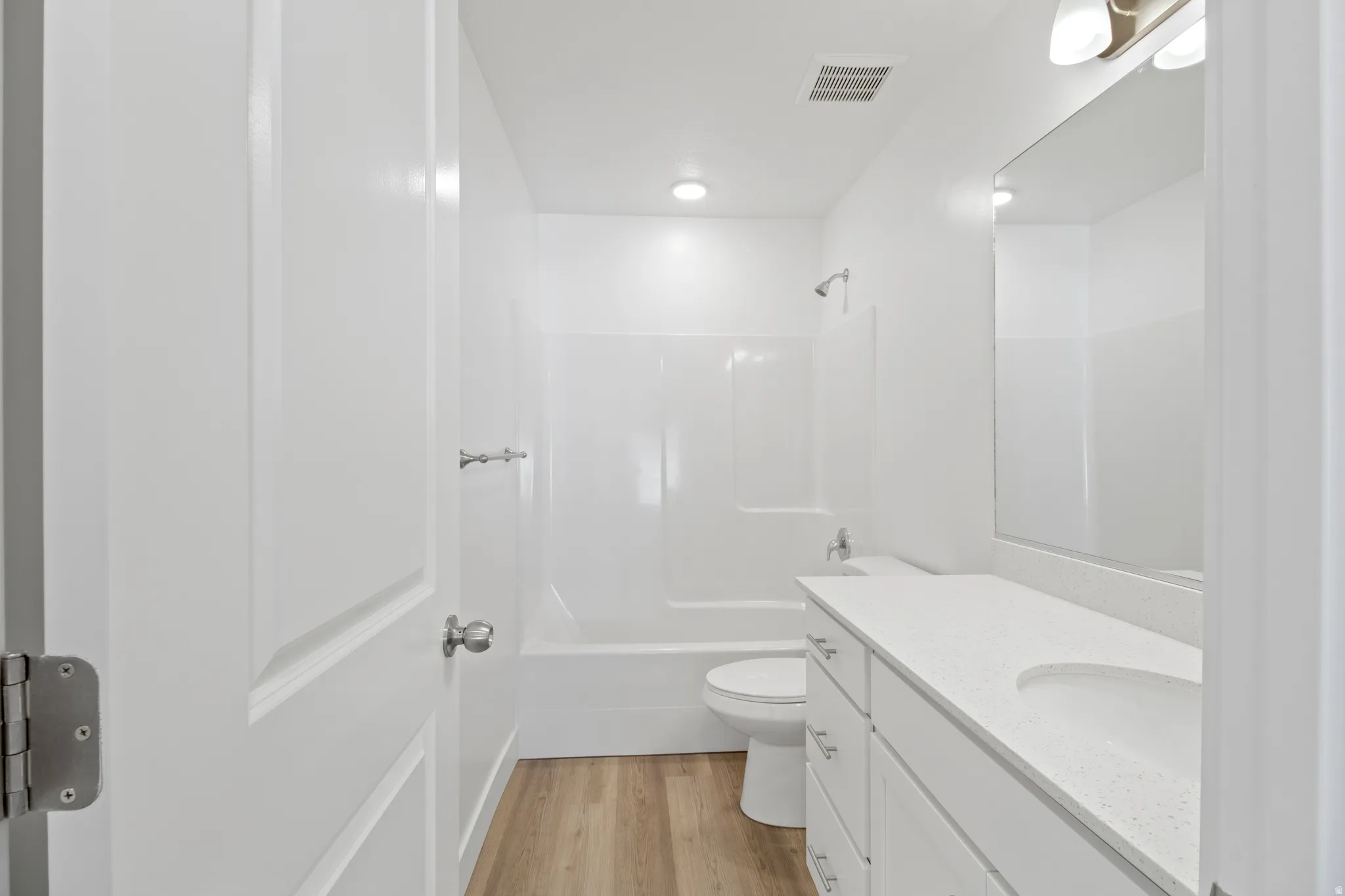 Bathroom featuring a white vanity with an integrated sink, a large mirror, a white bathtub with shower, and wood-finish flooring