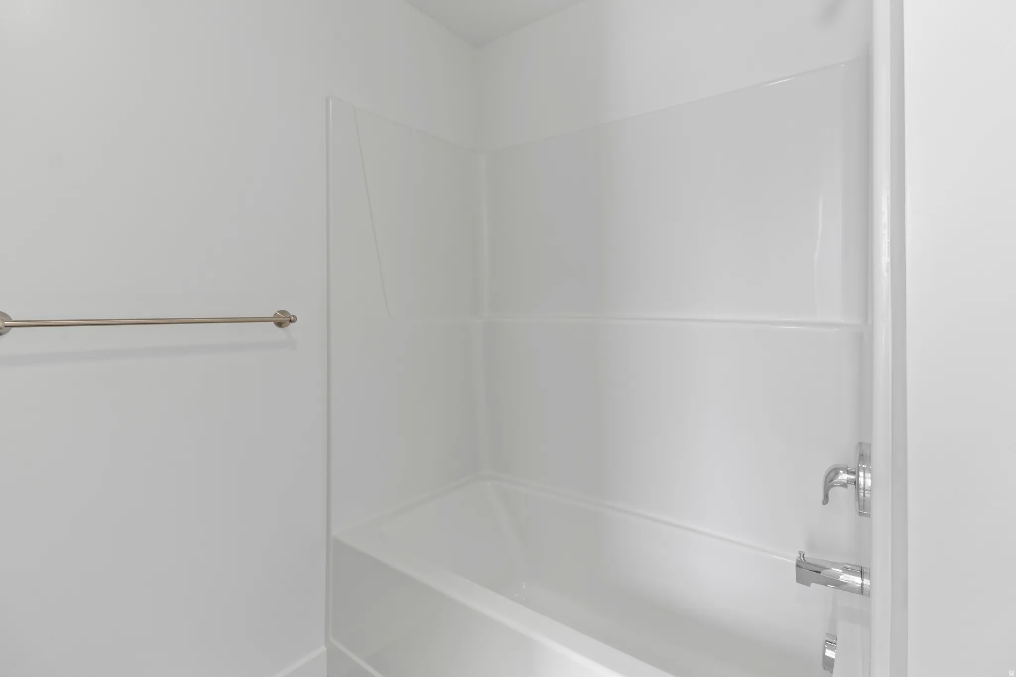 White bathtub with integrated shower surround, featuring chrome fixtures and a brushed nickel towel bar