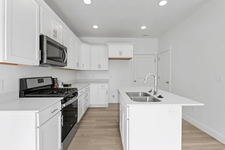 Modern kitchen with white cabinetry, stainless steel appliances, and light-toned wood-finish flooring