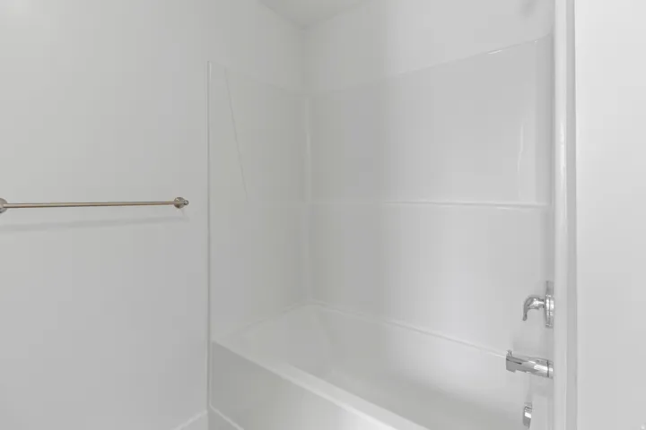 White bathtub with integrated shower surround, featuring chrome fixtures and a brushed nickel towel bar