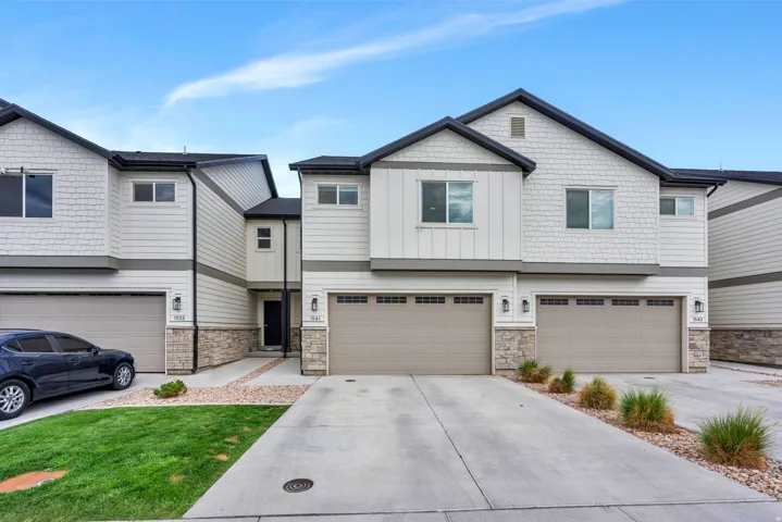 Contemporary townhome exterior featuring light-toned siding, dark trim, a two-car garage, stone accents, and a concrete driveway