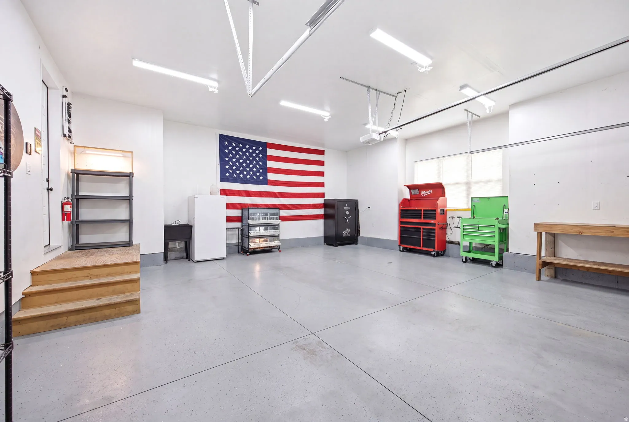 Spacious garage featuring a concrete floor, bright overhead lighting, white walls, and a large window providing natural illumination