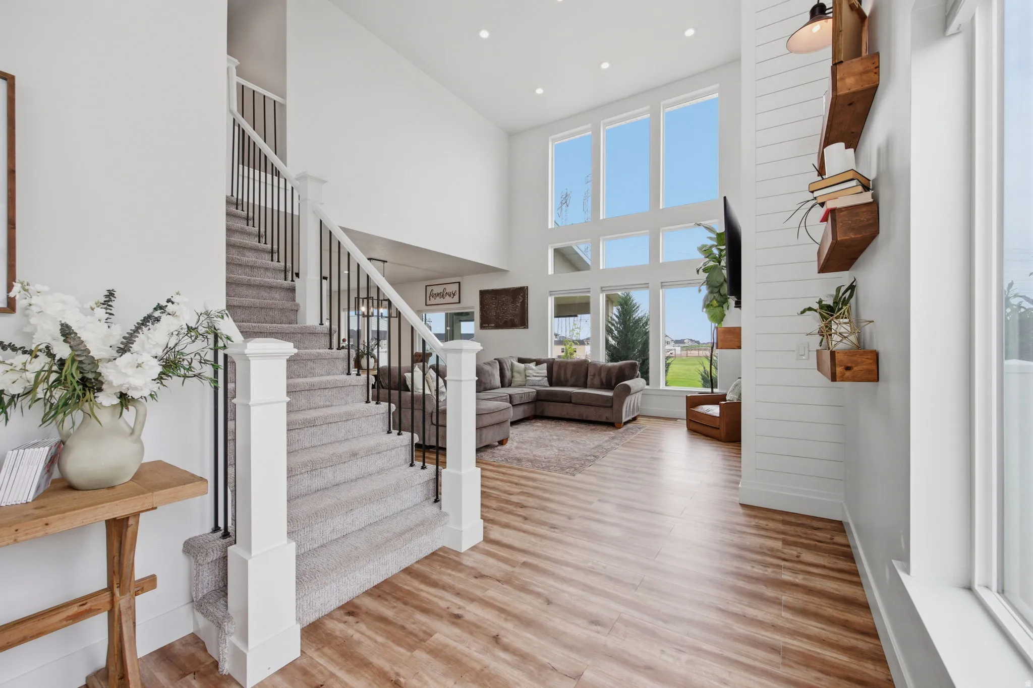 Two-story living area featuring wood-finish flooring and a carpeted staircase with white newel posts and black wrought iron balusters