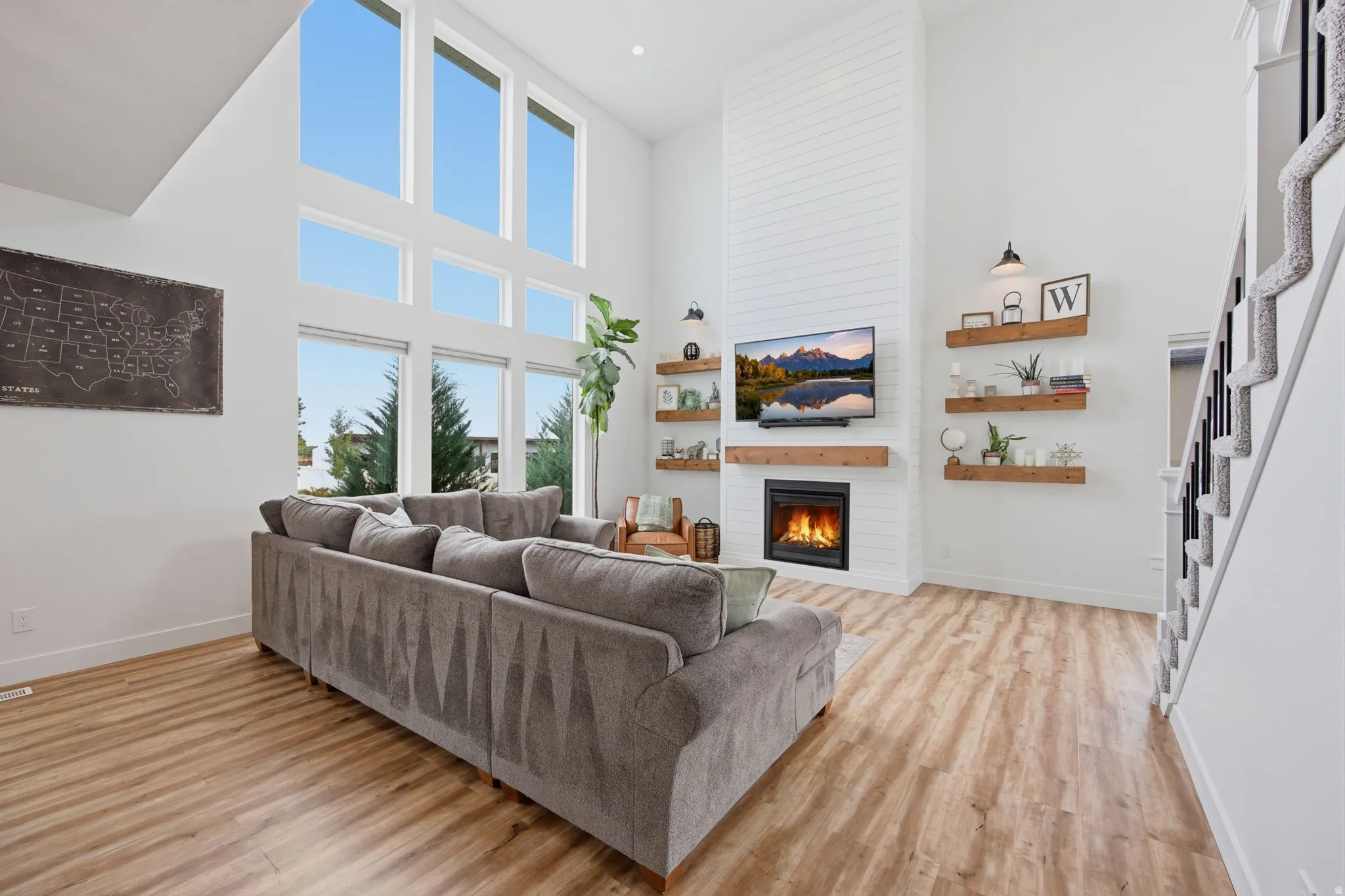 Two-story living area featuring tall windows, wood-finish flooring, a contemporary fireplace with a shiplap accent wall, built-in floating shelves, and a carpeted staircase with dark iron balusters