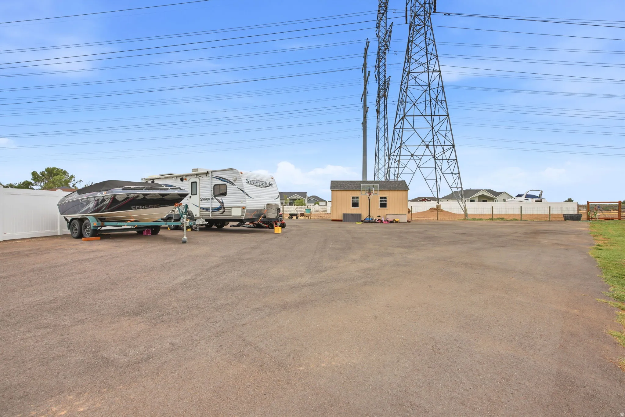 Expansive paved lot with a white privacy fence and a detached storage shed