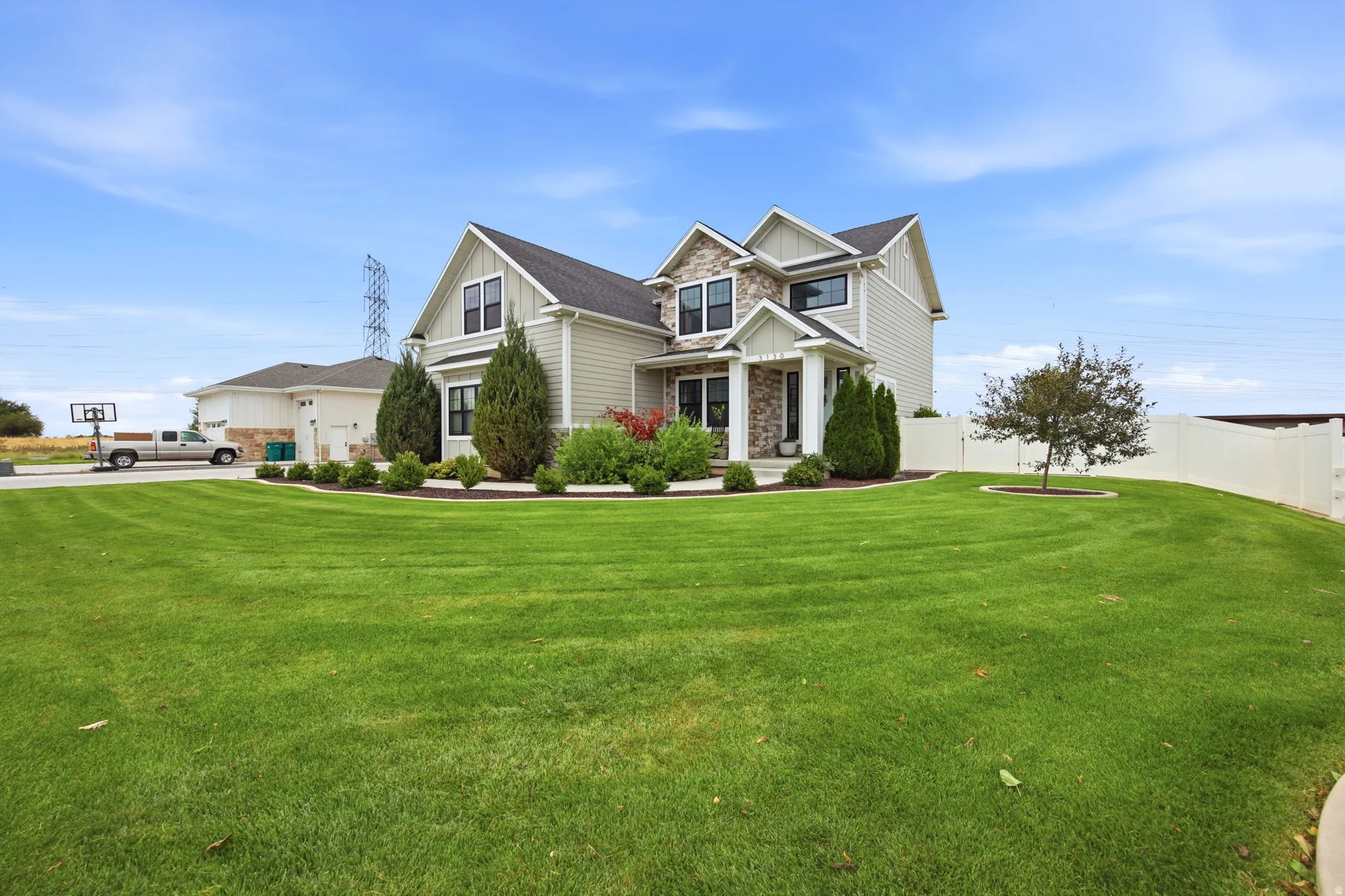 Contemporary two-story residence featuring a stone and siding facade, a covered front porch, and a fenced perimeter