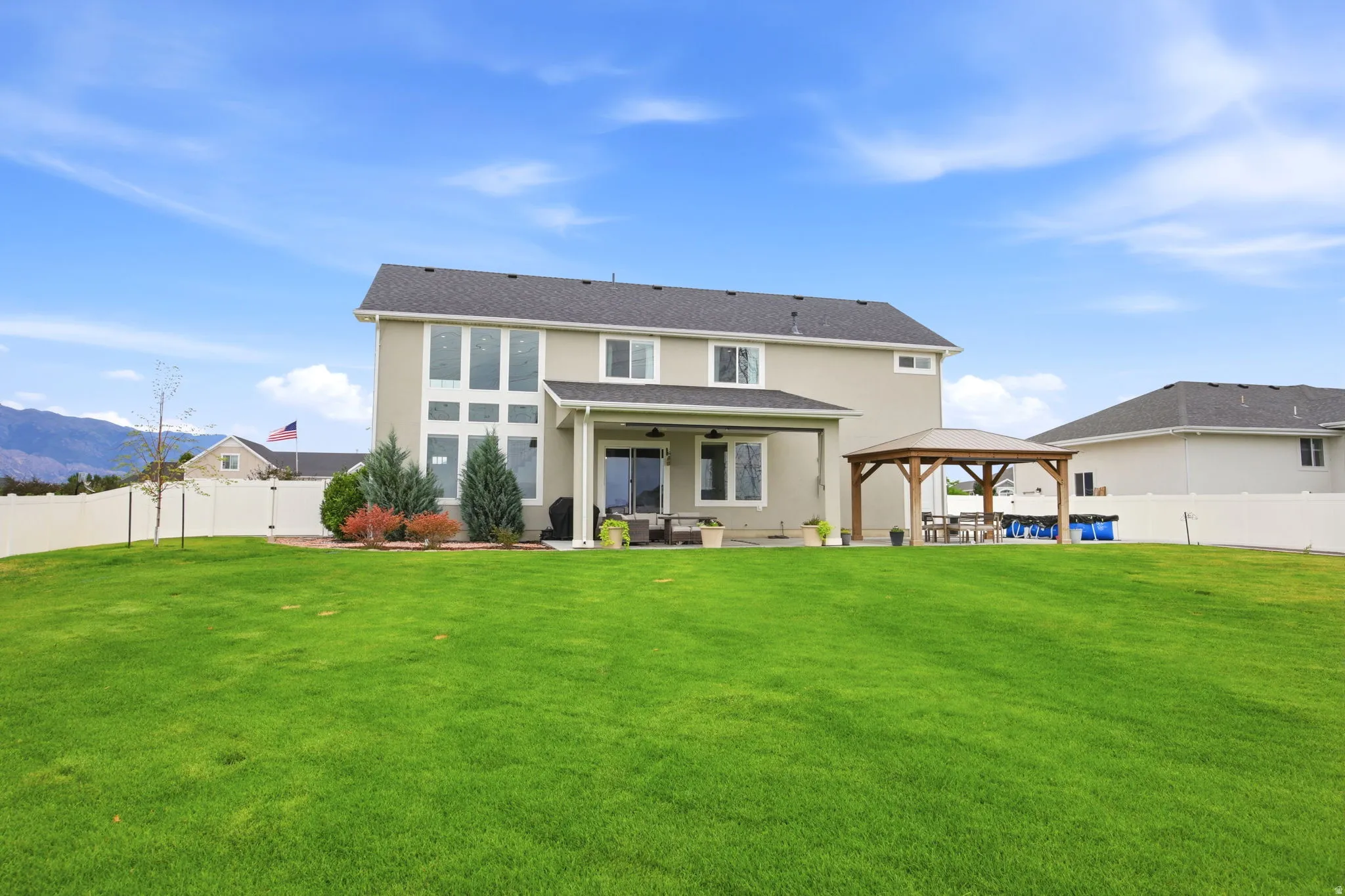 Expansive backyard with a manicured lawn, full vinyl fencing, and a permanent wooden gazebo