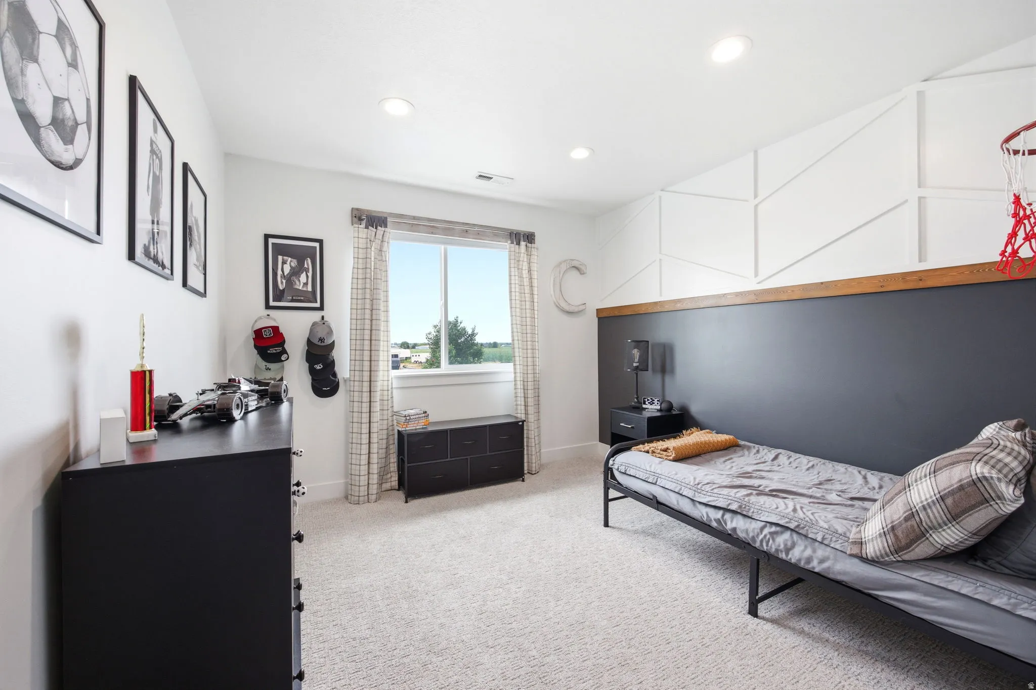 Spacious room featuring light-colored carpeting, recessed lighting, a large window with exterior scenery, a feature wall with a geometric panel design, and a contrasting dark accent wall with a wood-finish top trim