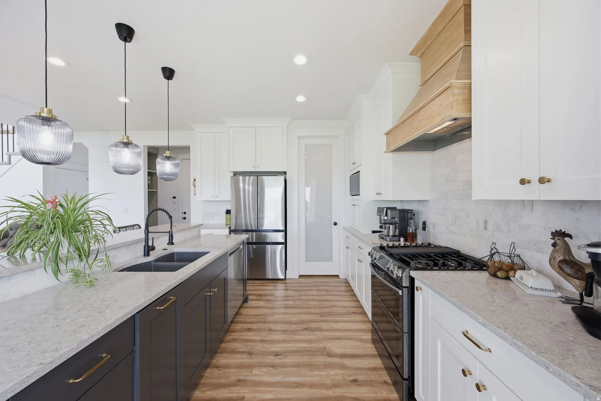 Contemporary kitchen featuring wood-finish flooring, light-toned countertops, white upper cabinetry, and a dark-toned island with a black sink and faucet