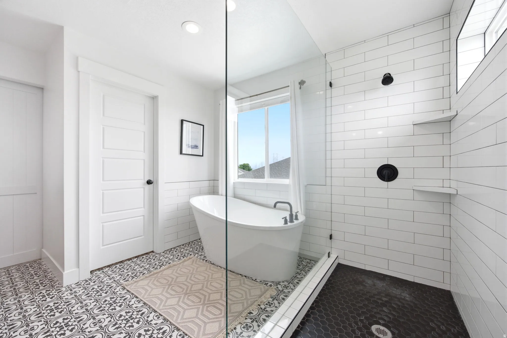 Freestanding soaking tub and walk-in shower with black hexagonal tile flooring and subway tile walls