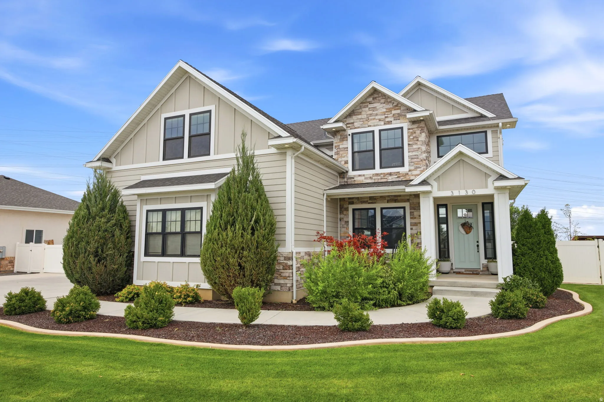 Two-story residence featuring light beige siding, stone facade accents, dark-framed windows, and a light blue front door