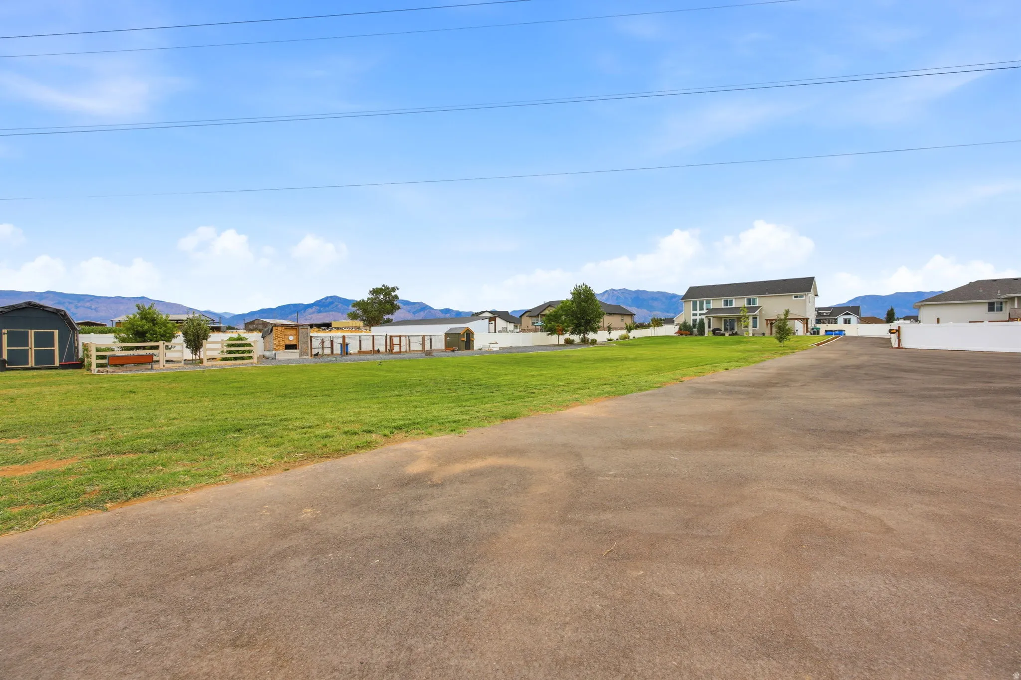 Expansive property featuring a paved driveway, a large grassy area, white fencing, and multiple outbuildings