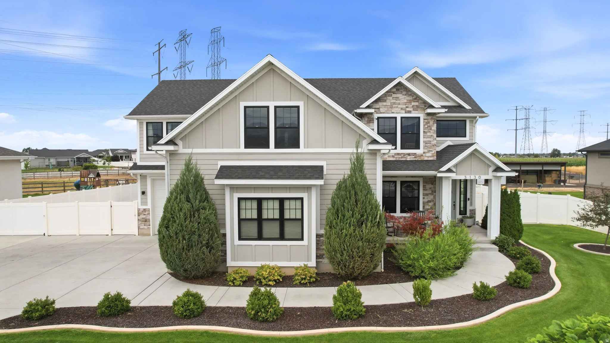 Modern farmhouse exterior with mixed material siding, stone accents, black-framed windows, and a concrete driveway
