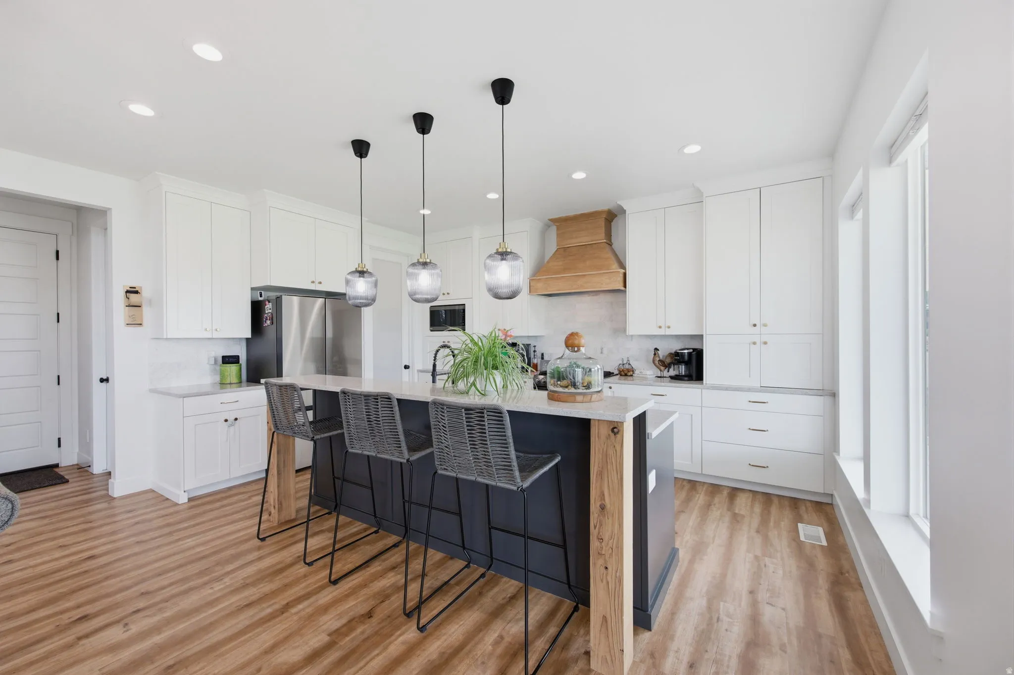 Contemporary kitchen featuring a large central island with seating, pendant lighting, white cabinetry, a wood-finish range hood, and stainless steel appliances