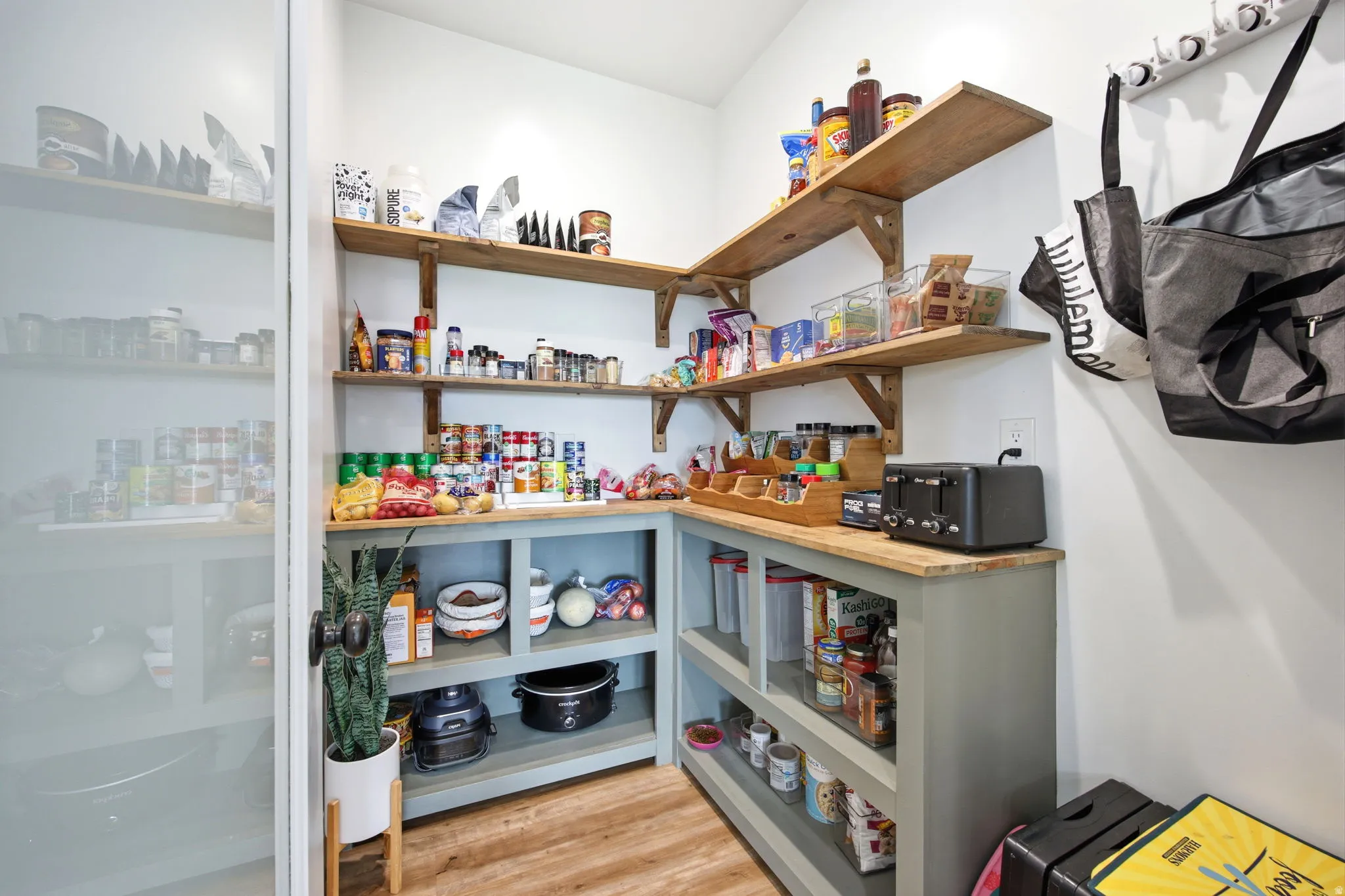 Spacious walk-in pantry featuring abundant wood shelving, a built-in countertop, lower cabinetry, and wood-finish flooring