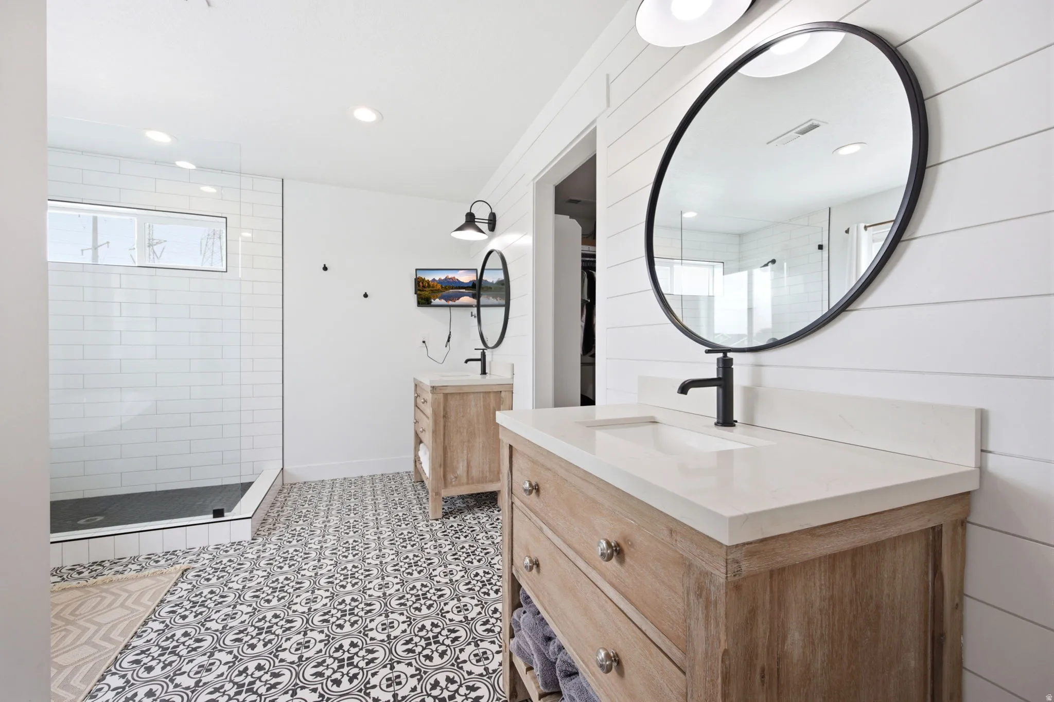 Modern bathroom featuring dual wood-finish vanities with light countertops and matte black fixtures