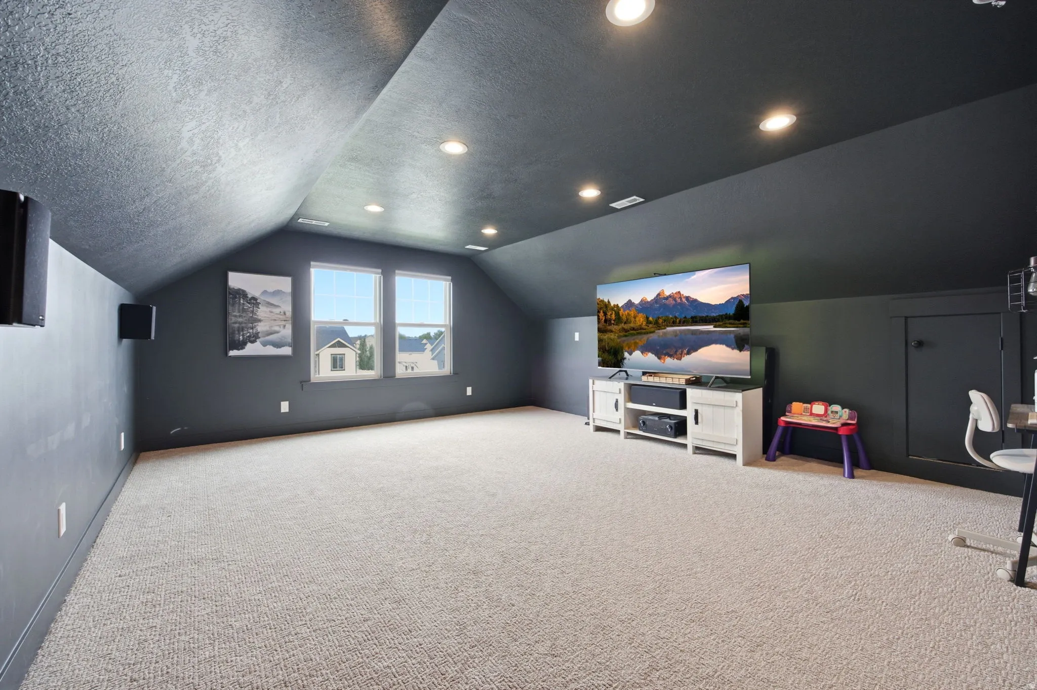 Spacious carpeted room featuring a sloped ceiling with recessed lighting