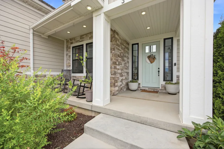 Inviting front porch featuring a light blue entry door with flanking sidelights, stone veneer accents, recessed lighting, and a concrete entry pad with steps