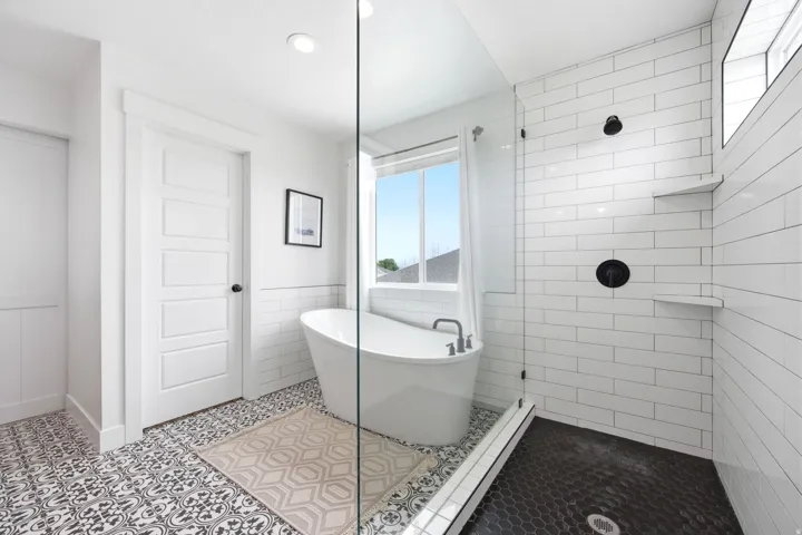 Freestanding soaking tub and walk-in shower with black hexagonal tile flooring and subway tile walls