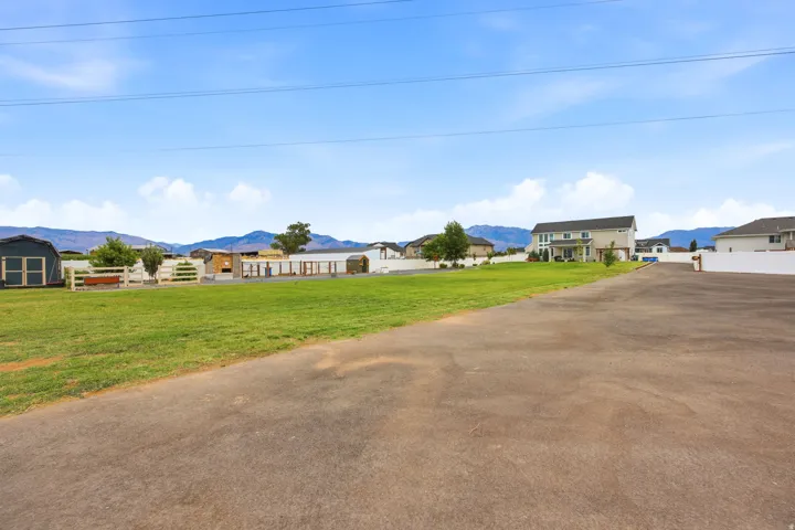 Expansive property featuring a paved driveway, a large grassy area, white fencing, and multiple outbuildings