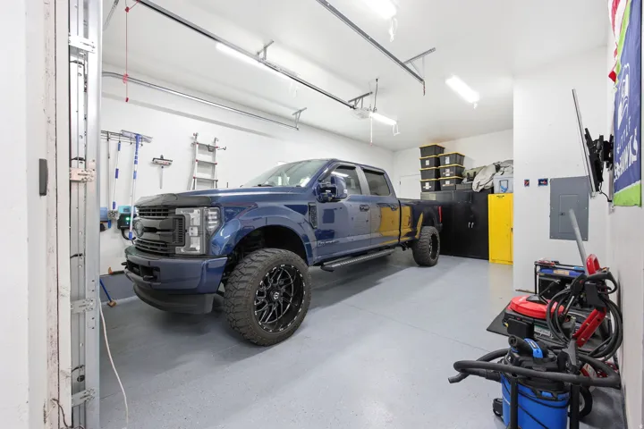 Spacious garage featuring a durable epoxy-coated floor, bright overhead fluorescent lighting, and overhead garage door tracks