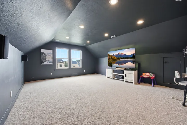 Spacious carpeted room featuring a sloped ceiling with recessed lighting