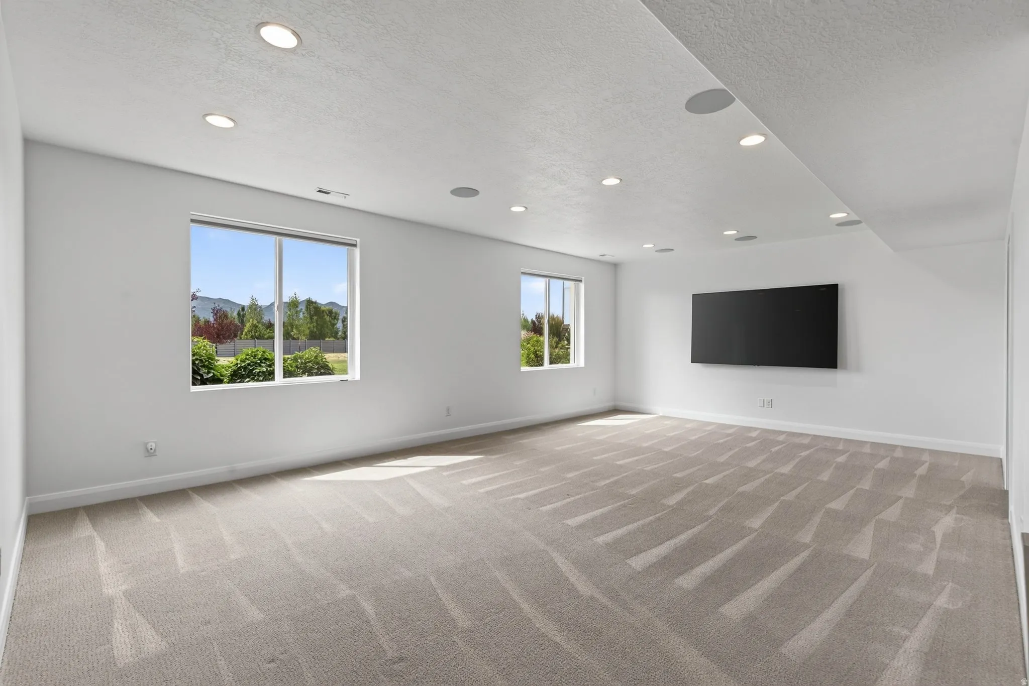 Spacious room featuring light-toned carpeting, recessed ceiling lighting, and multiple windows