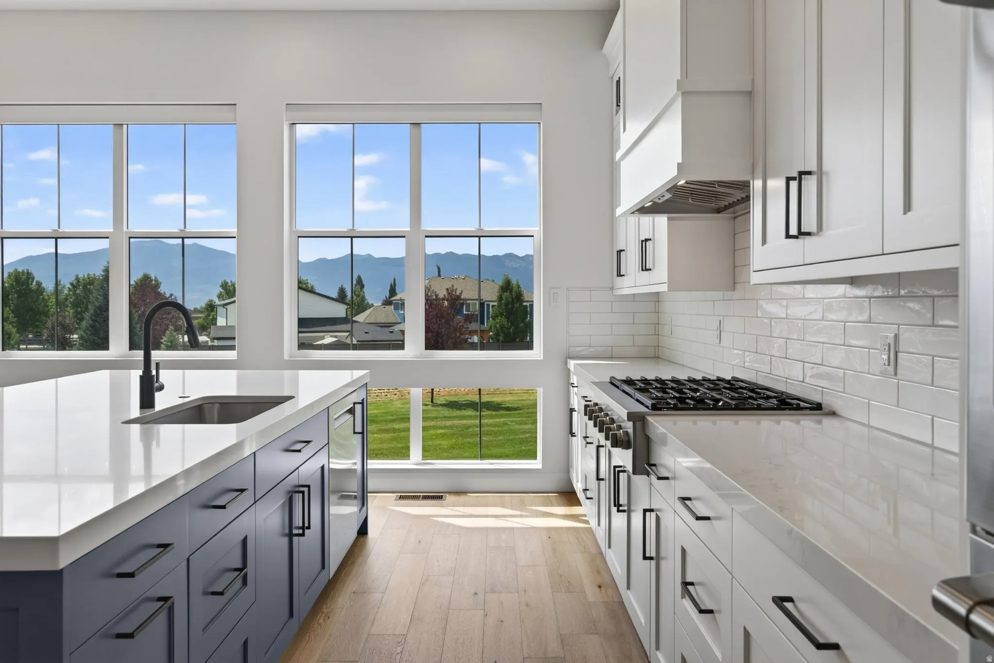Kitchen featuring an expansive island with an undermount sink and matte black faucet, light wood-finish flooring, white shaker cabinetry, and a subway tile backsplash