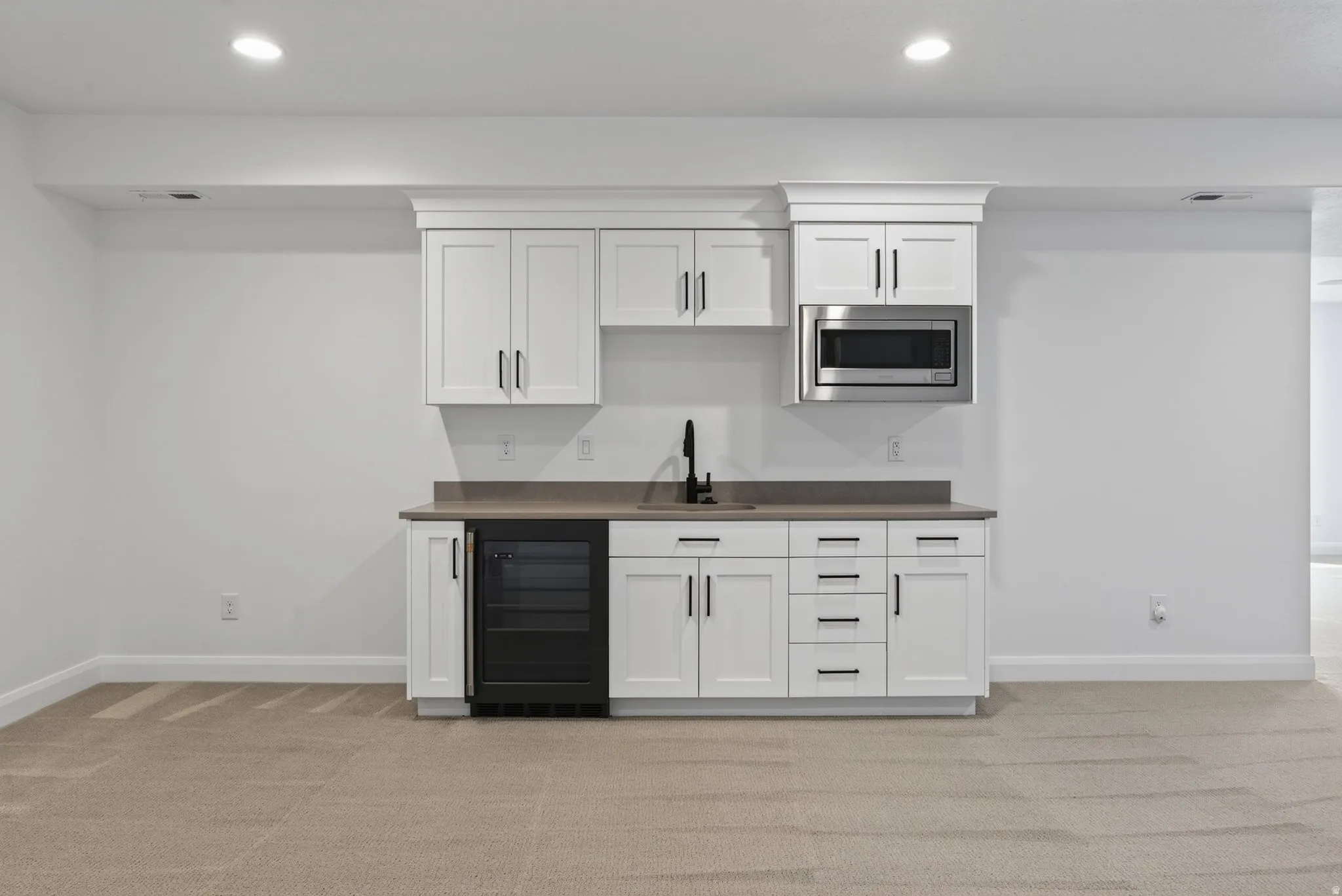 Built-in wet bar featuring white cabinetry, a stone-finish countertop, stainless steel microwave, black beverage refrigerator, and a matte black faucet