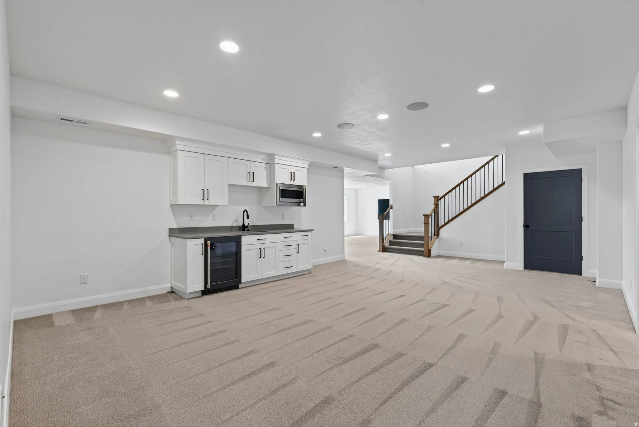 Spacious room featuring neutral carpeting, a built-in wet bar with white cabinetry, a sink, and a beverage cooler