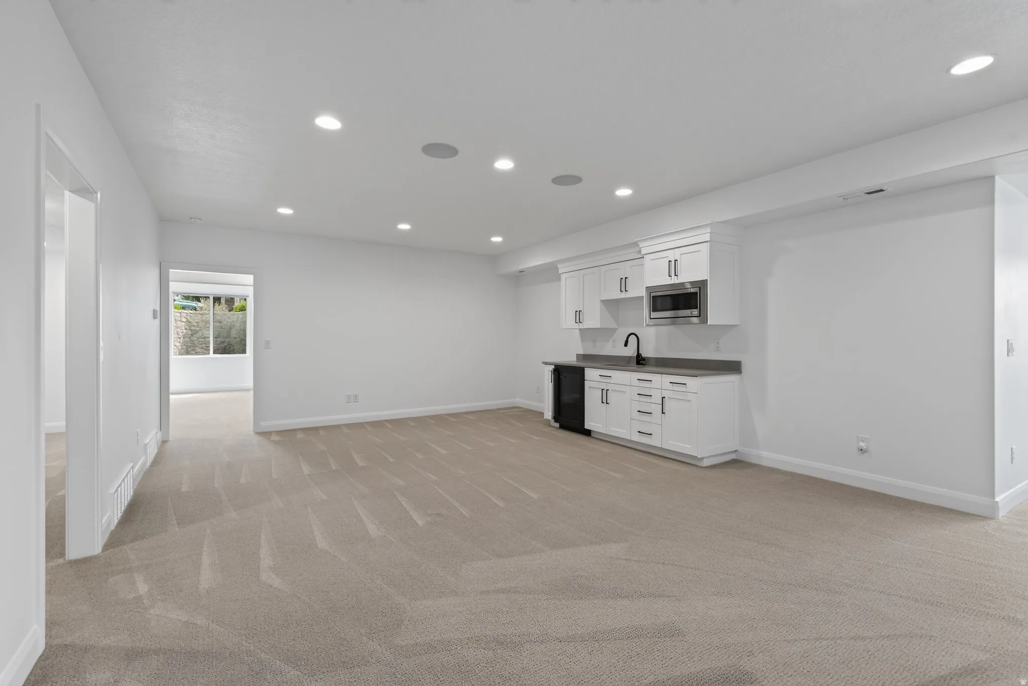 Spacious open-concept room featuring a built-in wet bar with white cabinetry, a black sink, and a stainless steel microwave