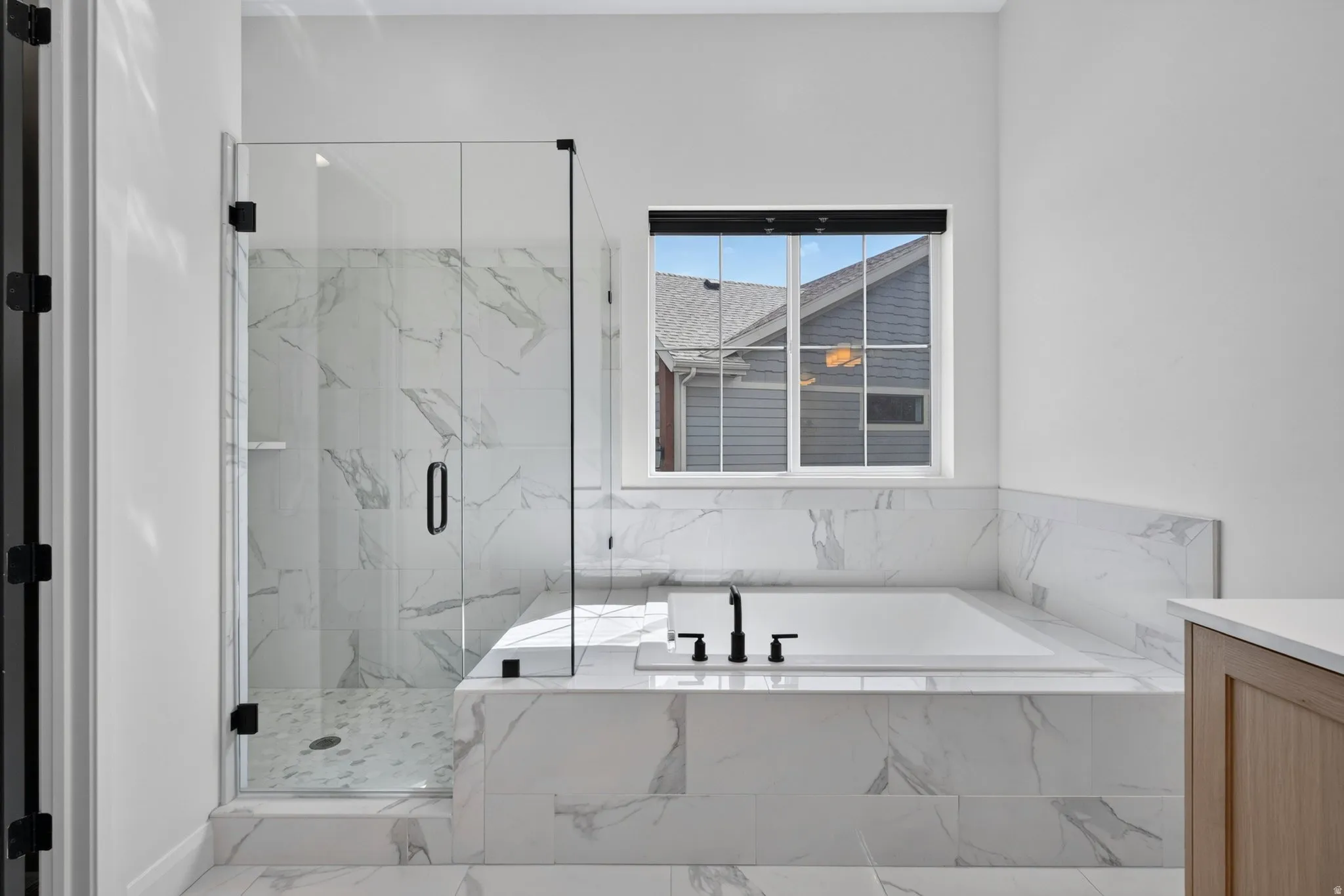 Sleek bathroom featuring a built-in soaking tub with matte black fixtures, a spacious walk-in shower with clear glass enclosure and patterned floor, and white marble-look tile surround
