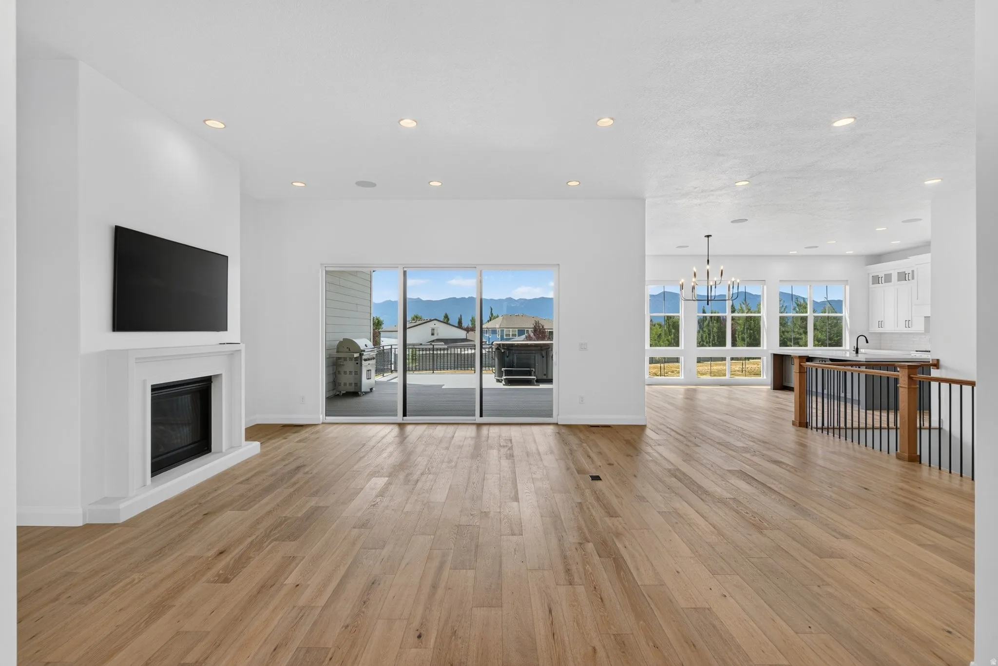 Spacious living area featuring wood-finish flooring, a white mantel fireplace, recessed lighting, and large sliding glass doors opening to the exterior