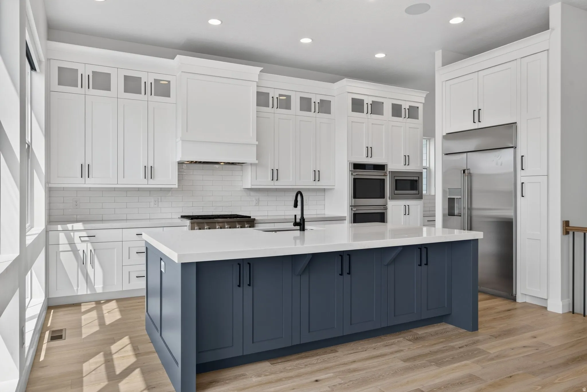 Kitchen featuring a large island with blue base cabinetry, white perimeter cabinetry, stainless steel appliances, and wood-finish flooring