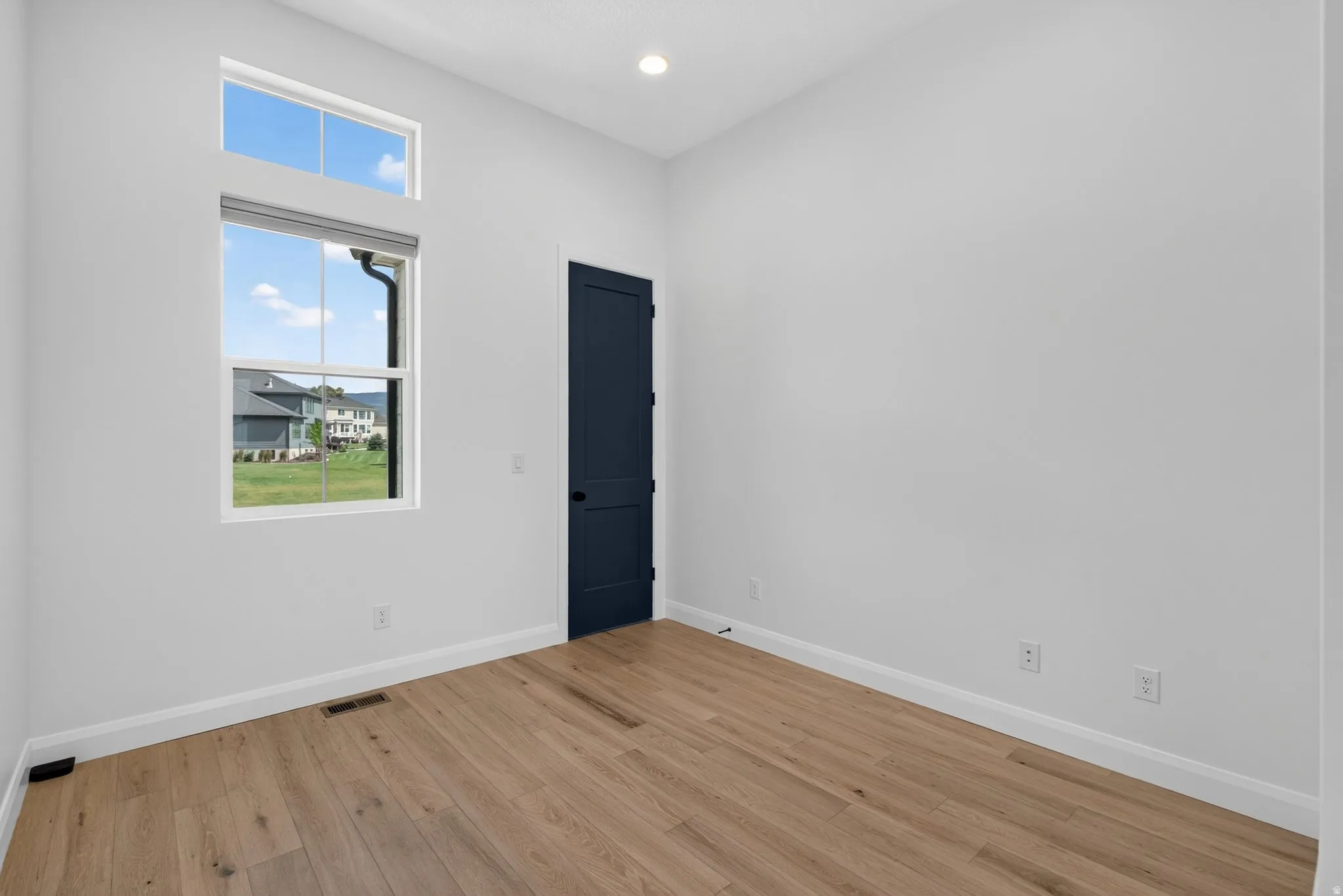 Bright room featuring light wood-finish flooring, a contemporary dark blue door, and a large window with an upper transom