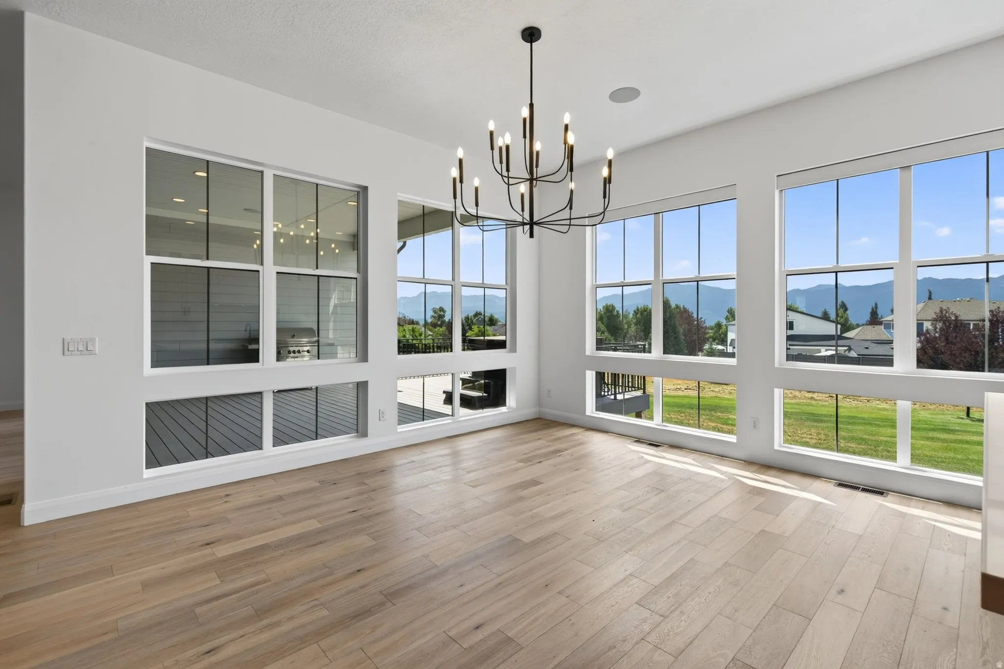 Spacious room featuring extensive window-lines, natural wood-finish flooring, and a contemporary black chandelier