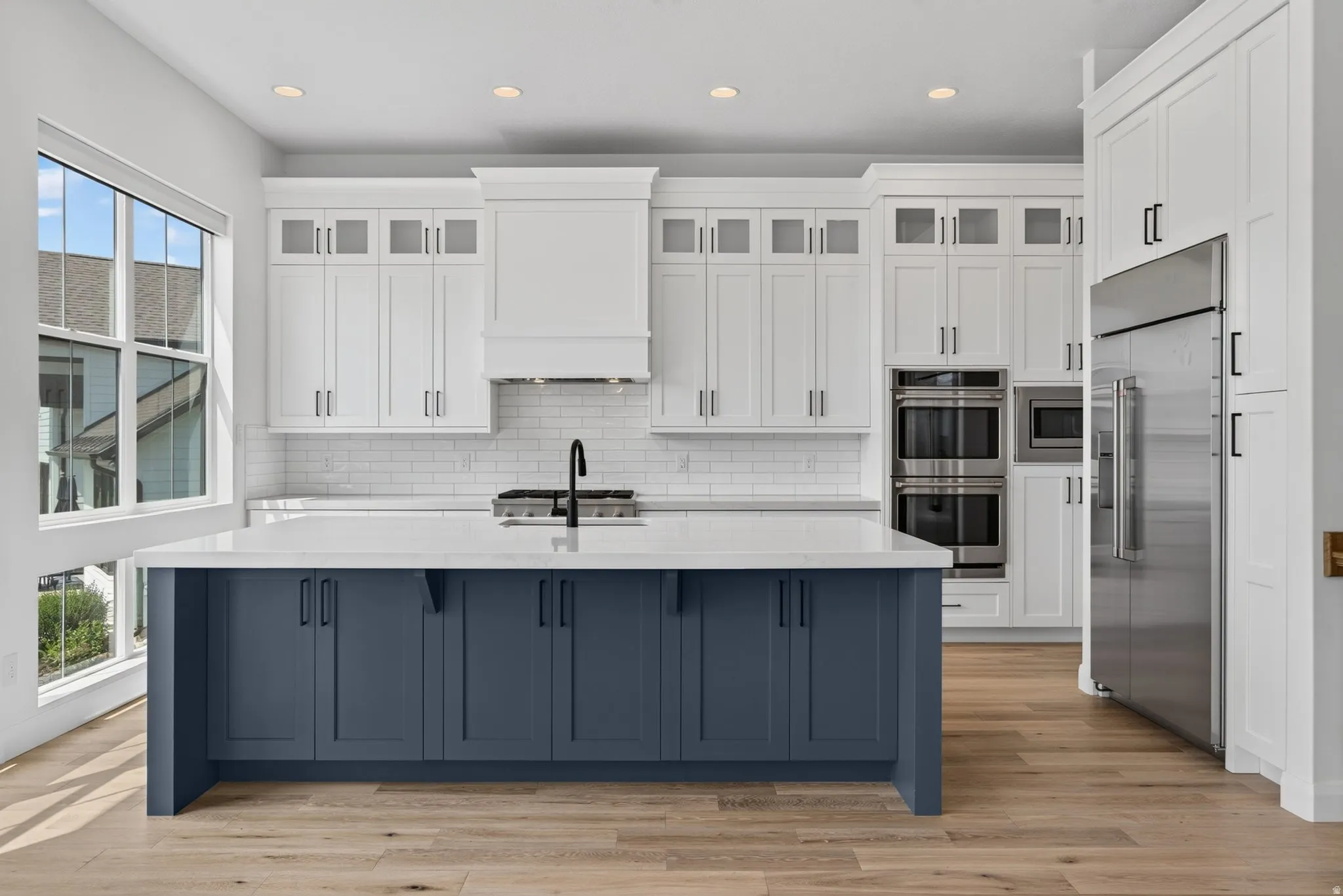 Modern kitchen featuring a large central island with blue cabinetry, light countertops, and wood-finish flooring