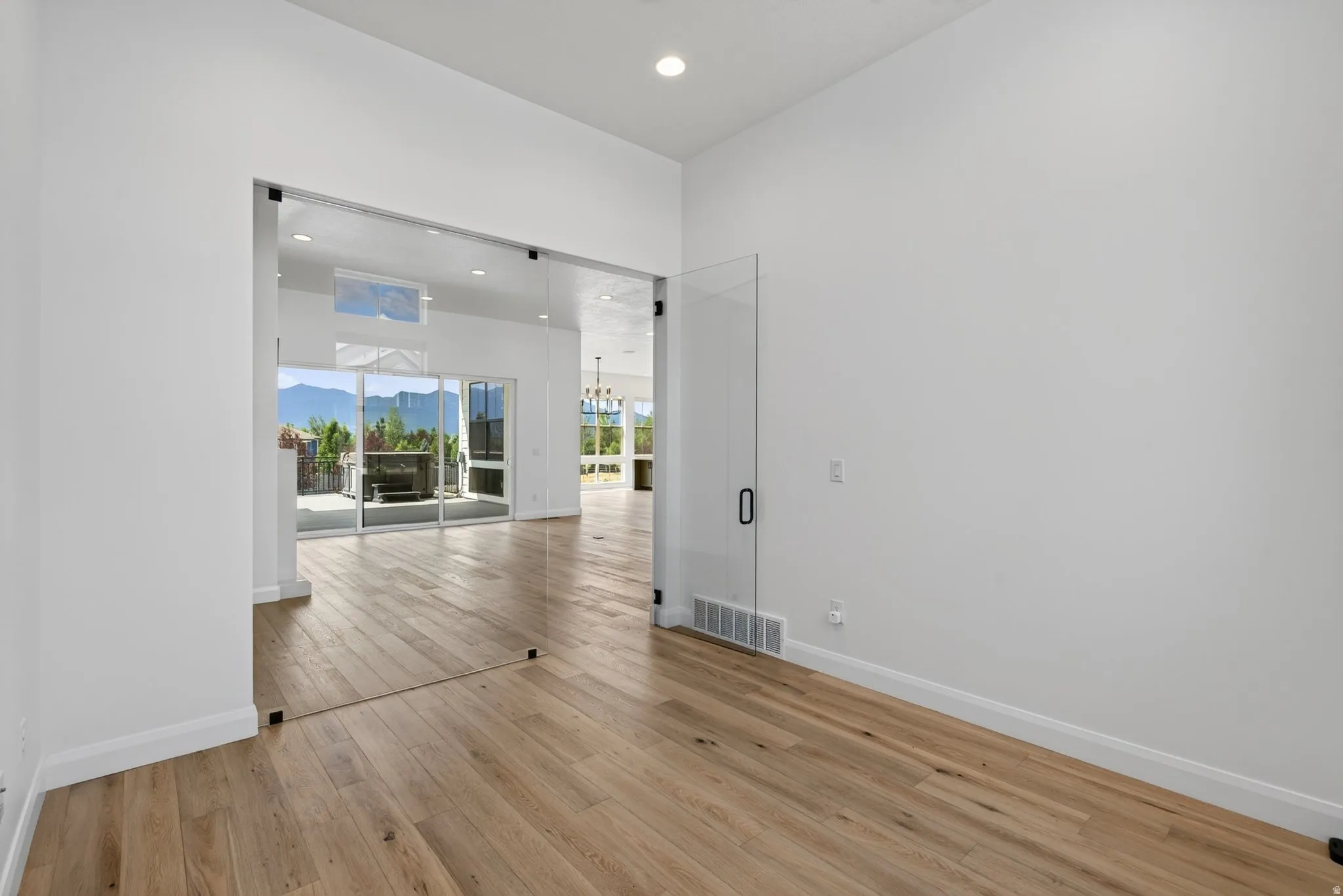 Interior space featuring full-height glass panel entry, wood-finish flooring, recessed lighting, and white walls