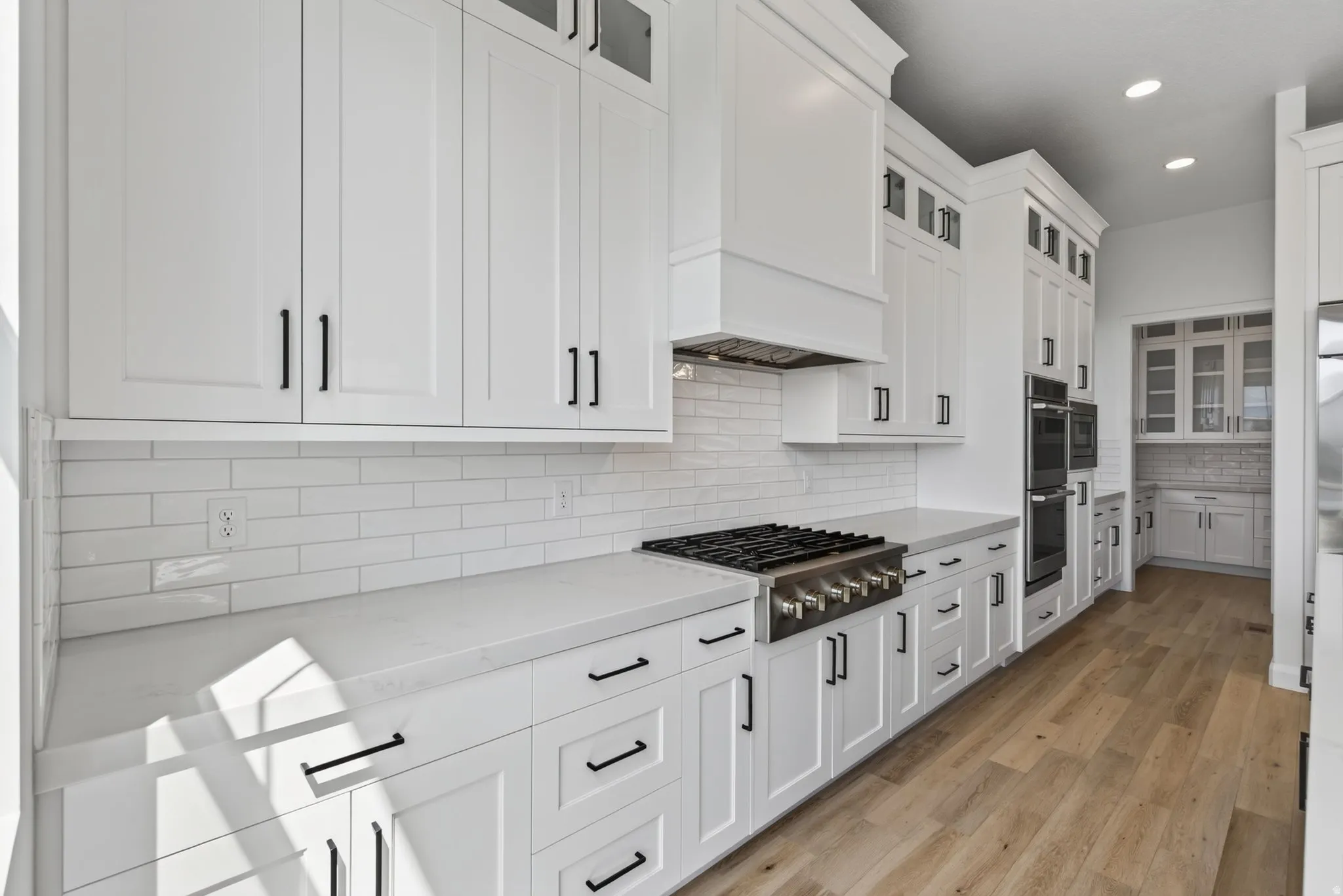 Modern kitchen featuring white shaker cabinetry with black hardware, white subway tile backsplash, and light-toned countertops