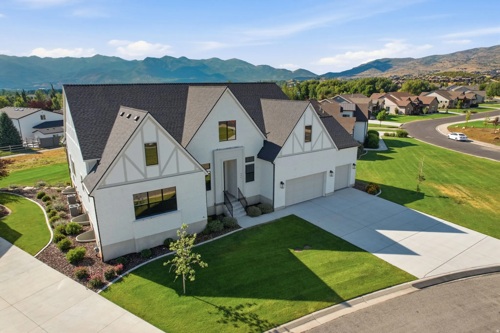 Modern Tudor-style residence featuring a white stucco exterior, black-framed windows, and a dark shingle roof