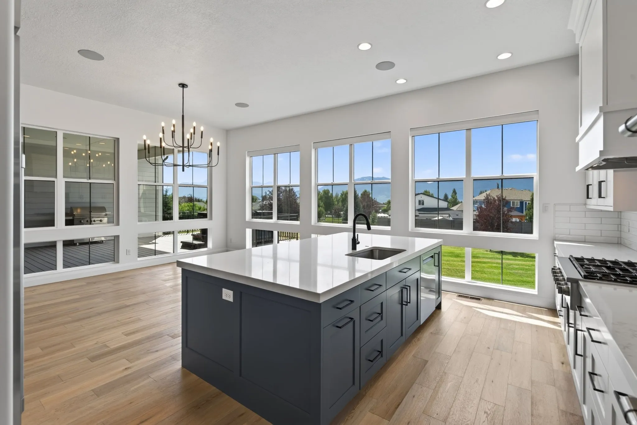 Bright kitchen featuring a central island with an integrated sink, expansive windows, light wood-finish flooring, white subway tile backsplash, and recessed lighting