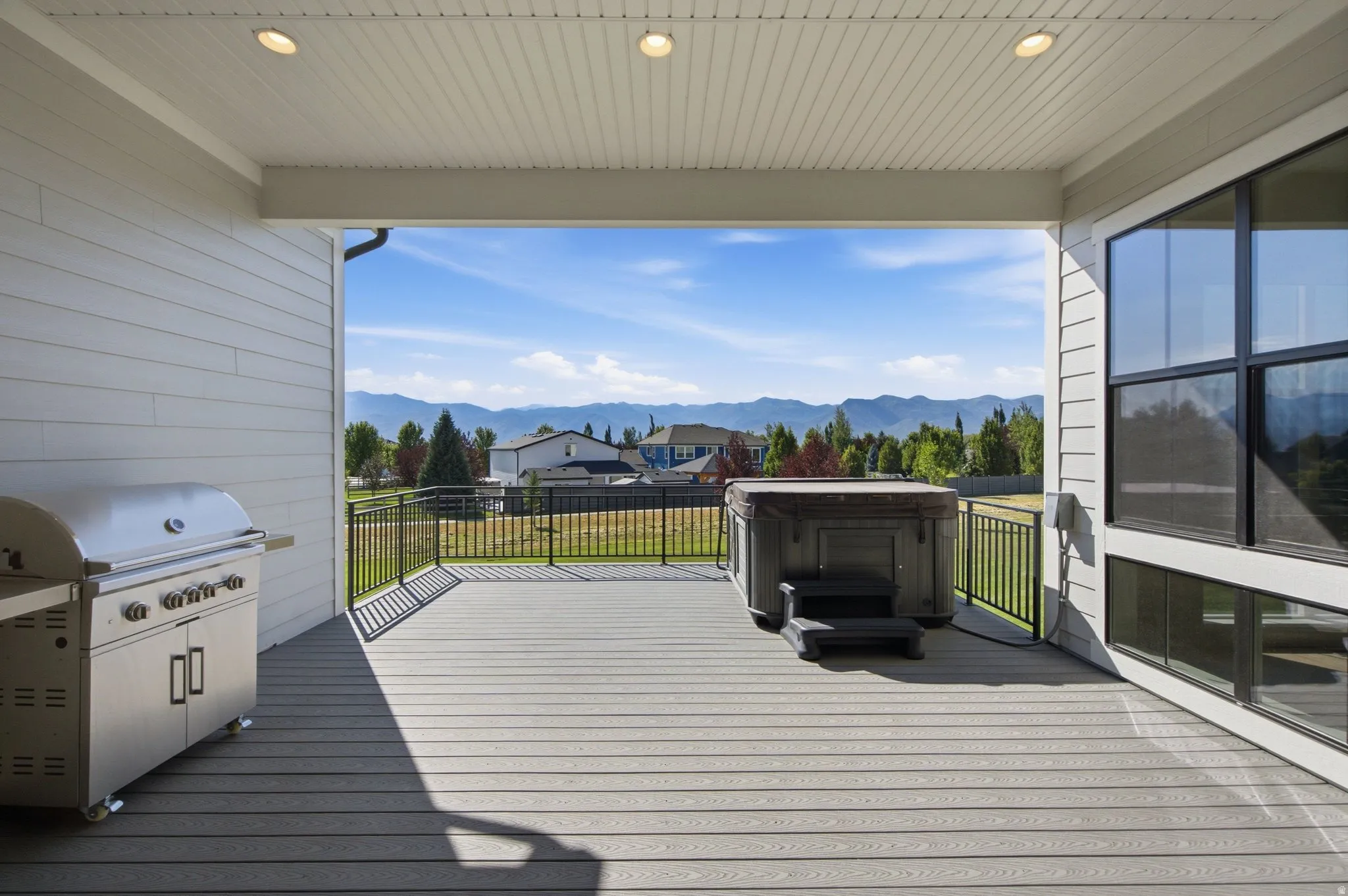 Covered composite deck featuring a hot tub, stainless steel barbecue grill, and black metal railings