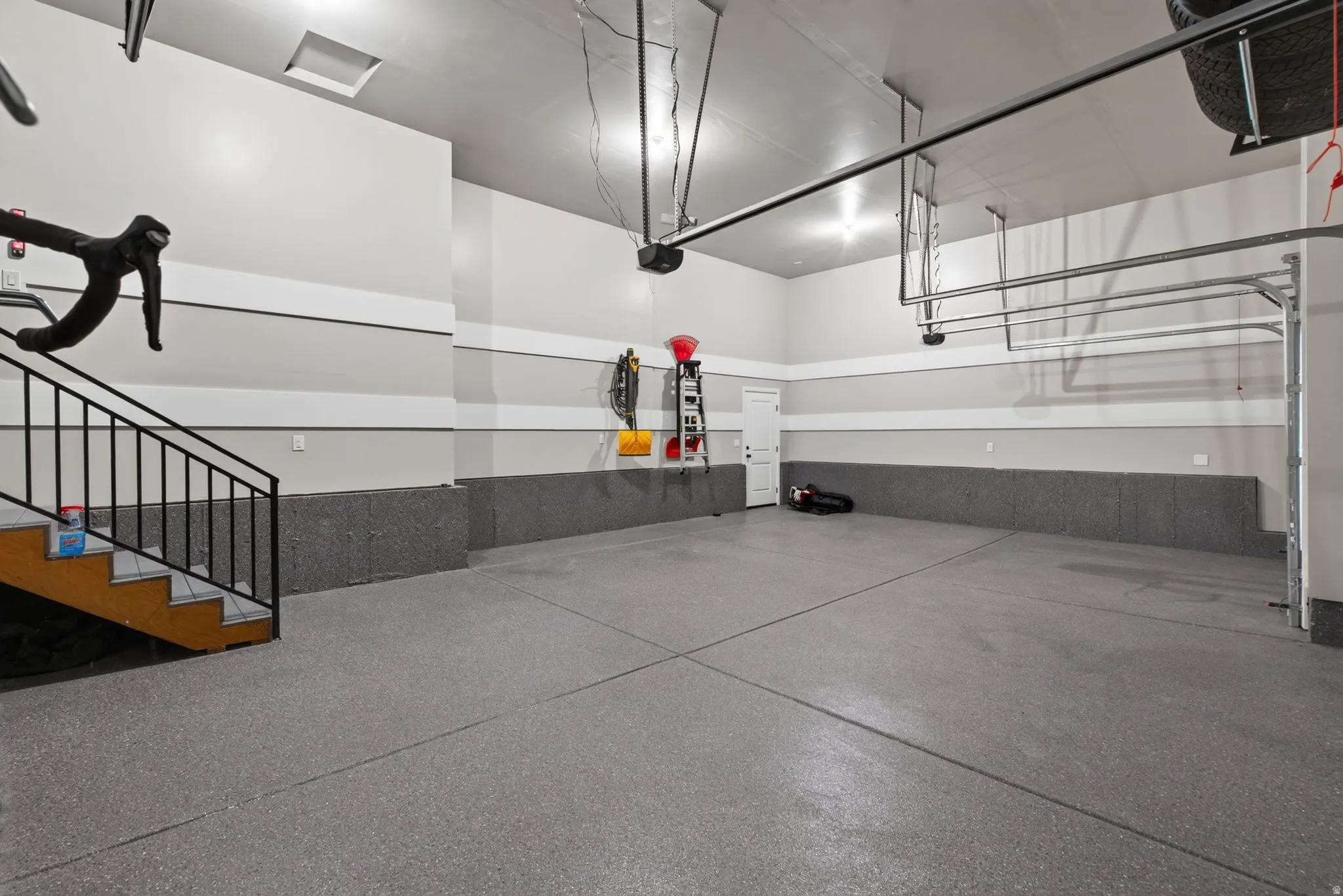 Spacious two-car garage with epoxy flooring, finished walls, and a staircase providing internal access