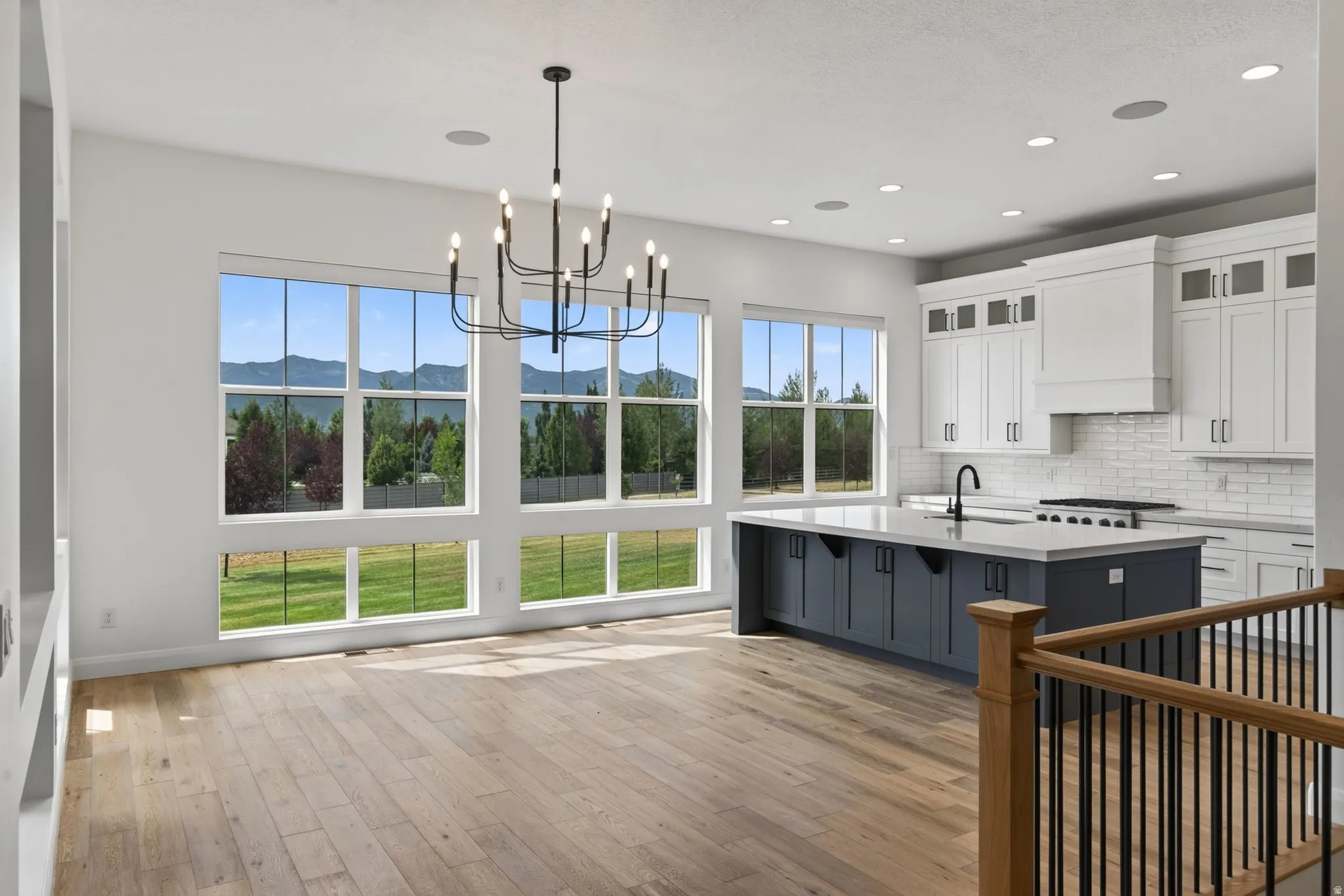 Open-concept living space featuring wood-finish flooring, a contemporary black chandelier, and multiple large windows