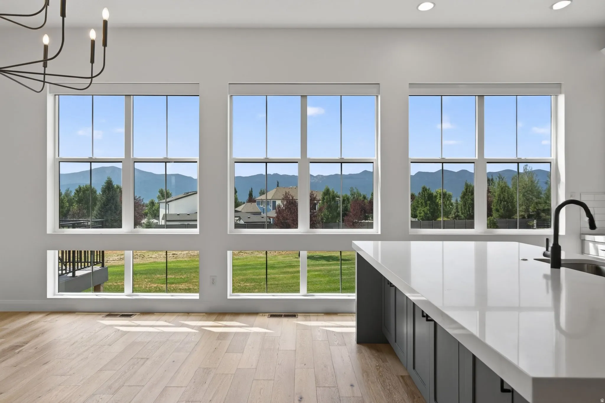 Spacious interior featuring large windows, wood-finish flooring, recessed lighting, and a kitchen island with a light-toned countertop and matte black faucet