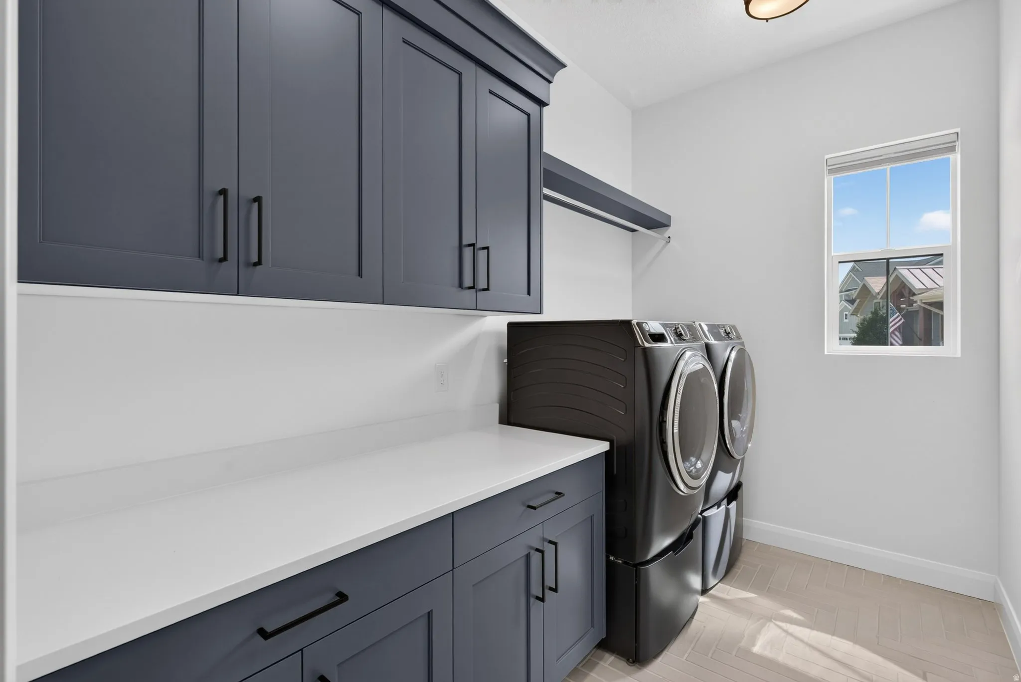Laundry room featuring dark shaker cabinetry, white countertops, built-in shelving, and light-toned herringbone tile flooring