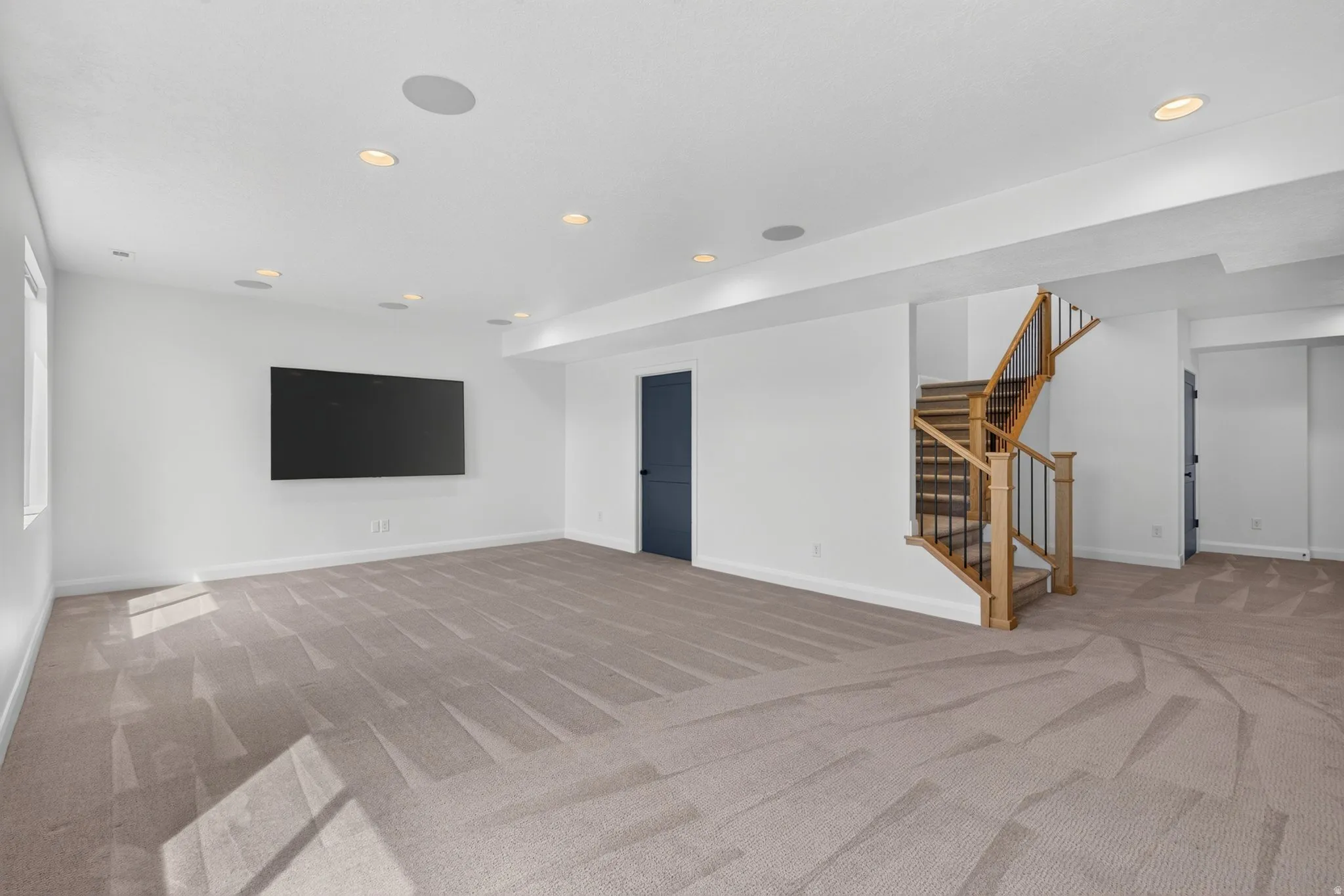 Spacious room featuring neutral carpeting, recessed ceiling lighting, and a wall-mounted display